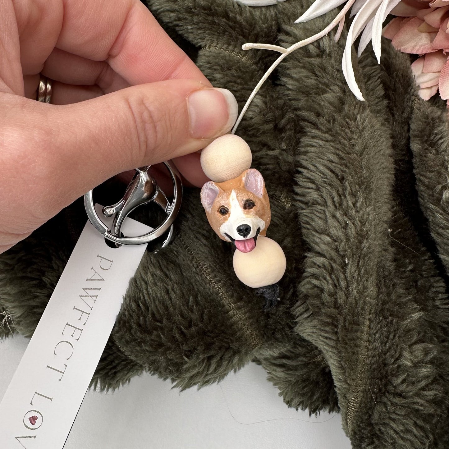 Corgi Dog-shaped keychain attached to a fluffy brown bag with a hand holding it.