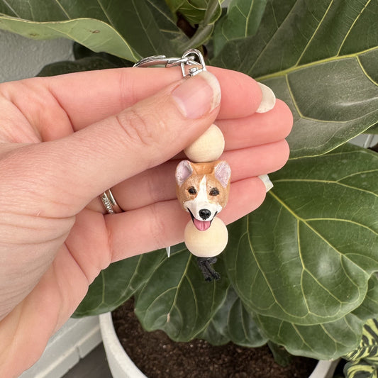 Hand holding a corgi dog-shaped keychain with a plant in the background
