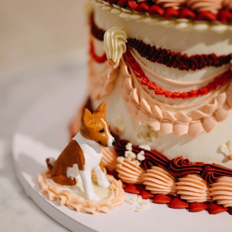 Custom pet cake topper of a basenji dog, beside a colourful lambeth style wedding cake.