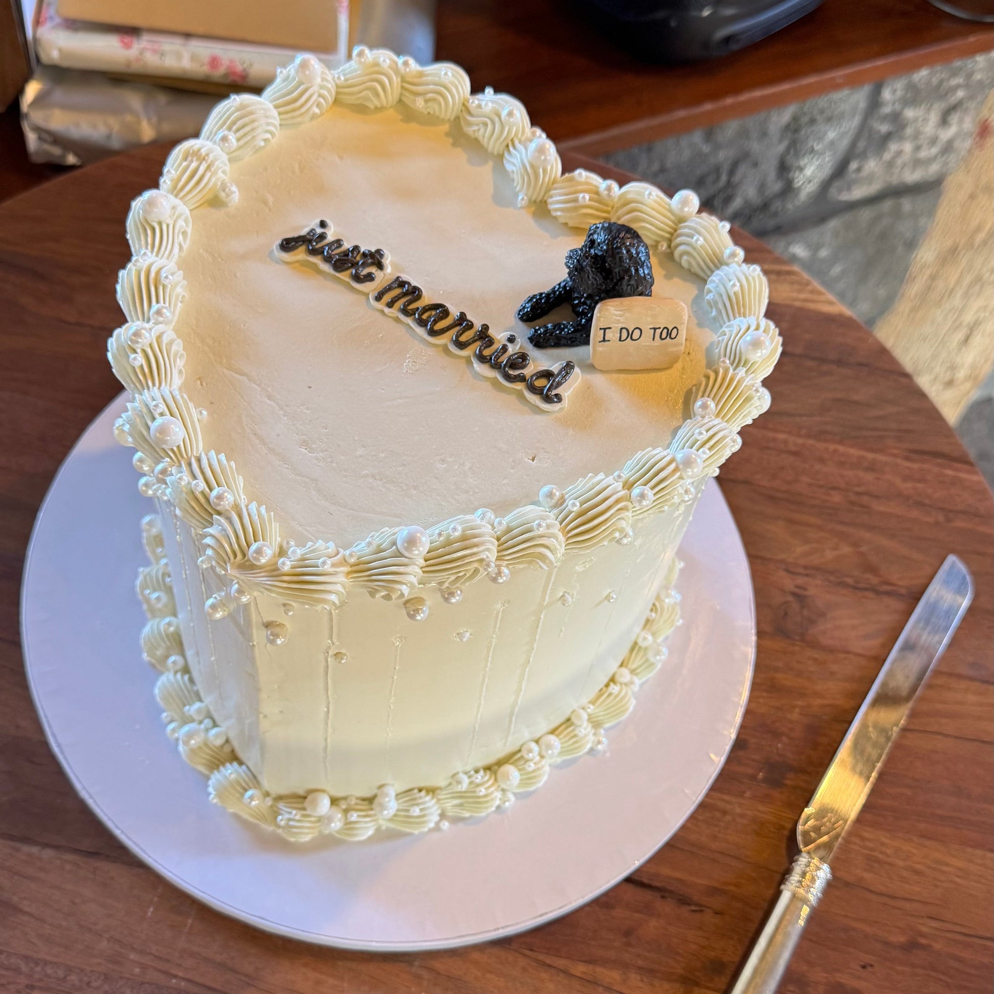 Heart-shaped wedding cake with 'just married' inscription on a wooden table with custom poodle peeking cake topper.
