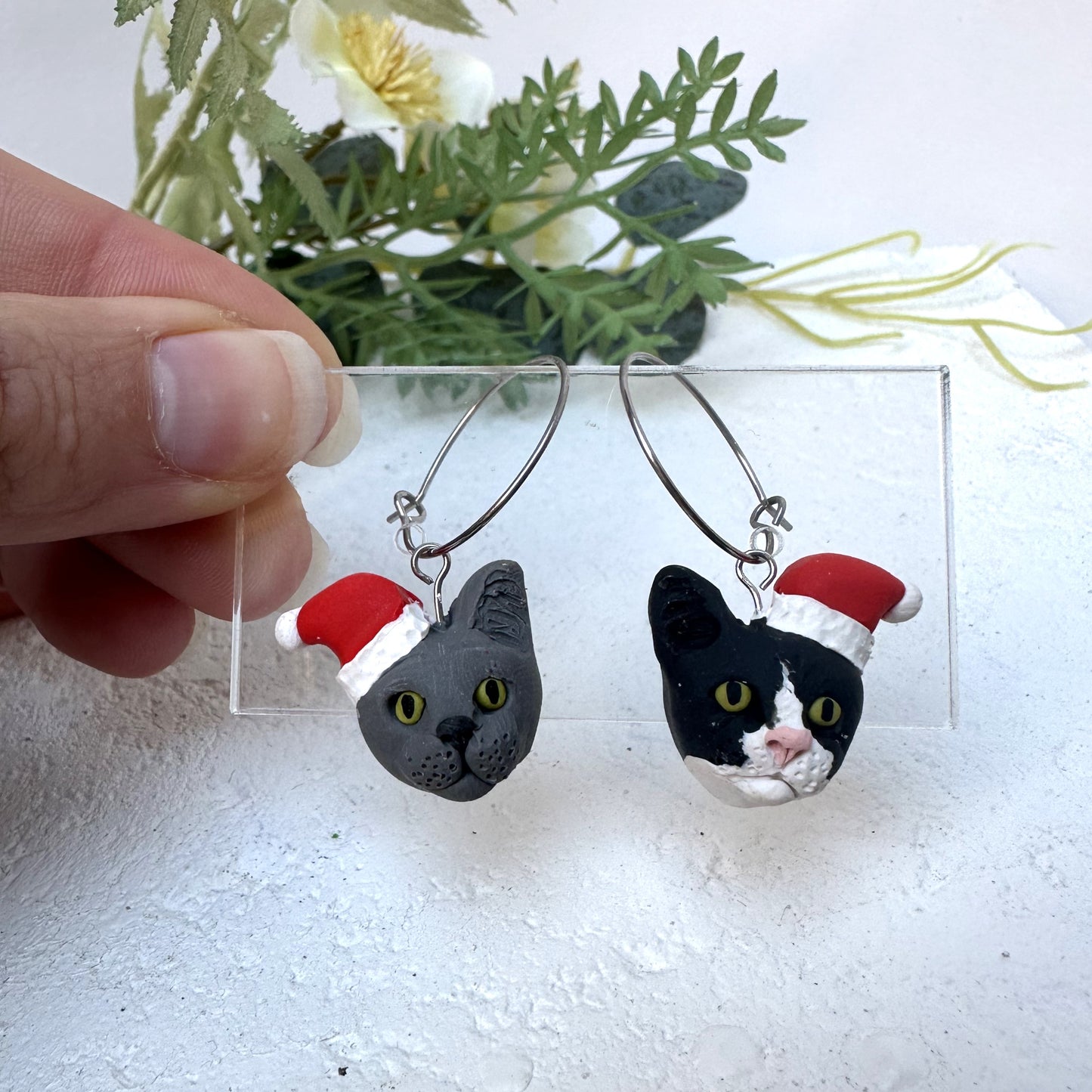 Handmade mismatched custom cat hoop earrings wearing santa hats.