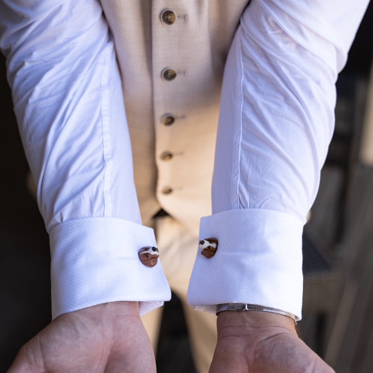 Close-up of a person wearing a white shirt with rolled-up sleeves and custom dog cufflinks.