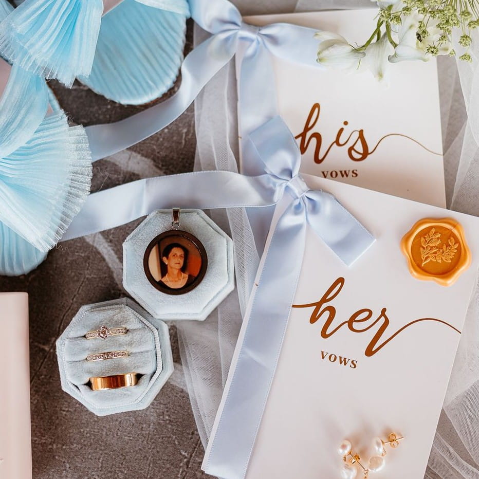 Wedding rings and accessories with 'his vows' and 'her vows' cards on a textured surface.