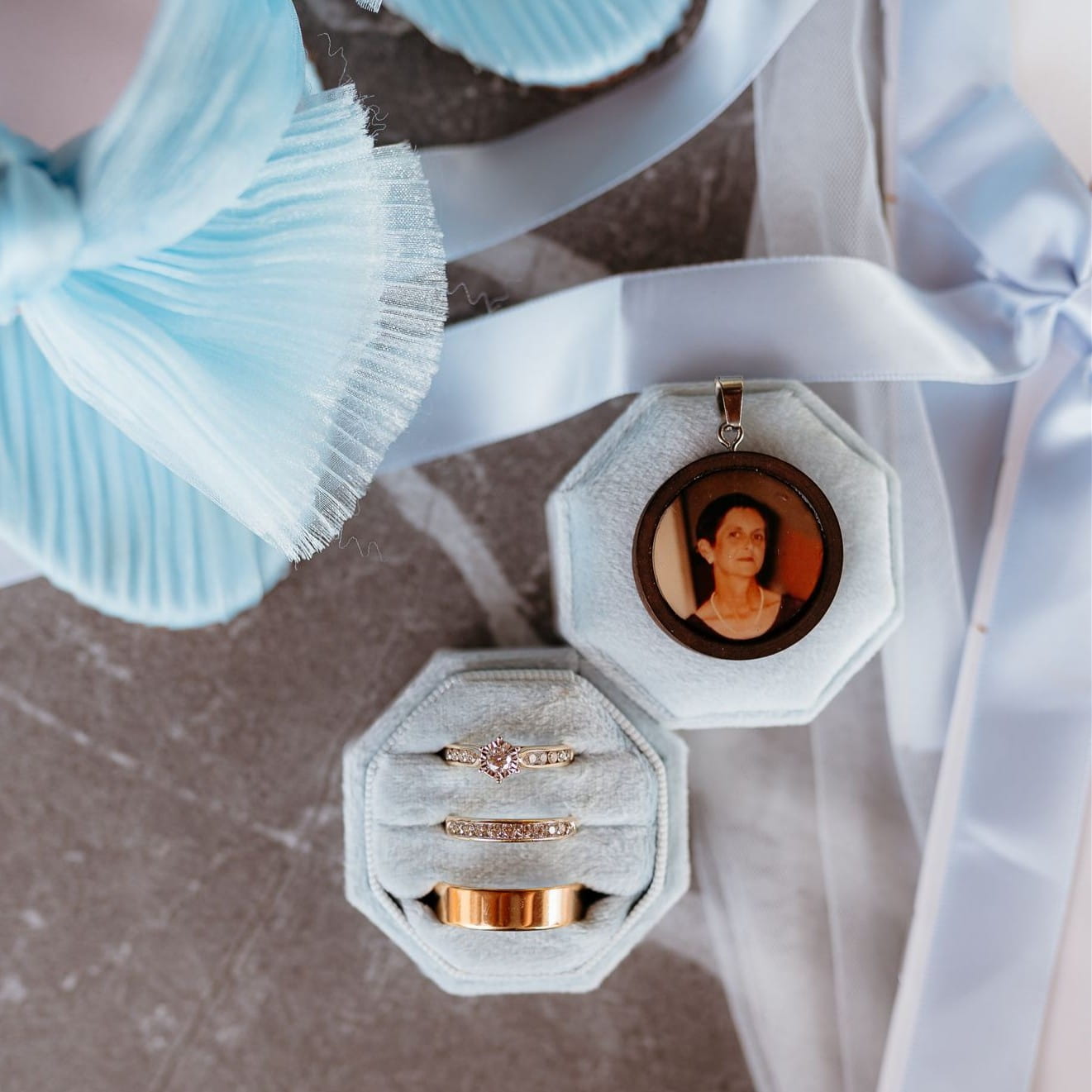 Two wedding rings in a decorative box with a portrait pendant on a textured surface.
