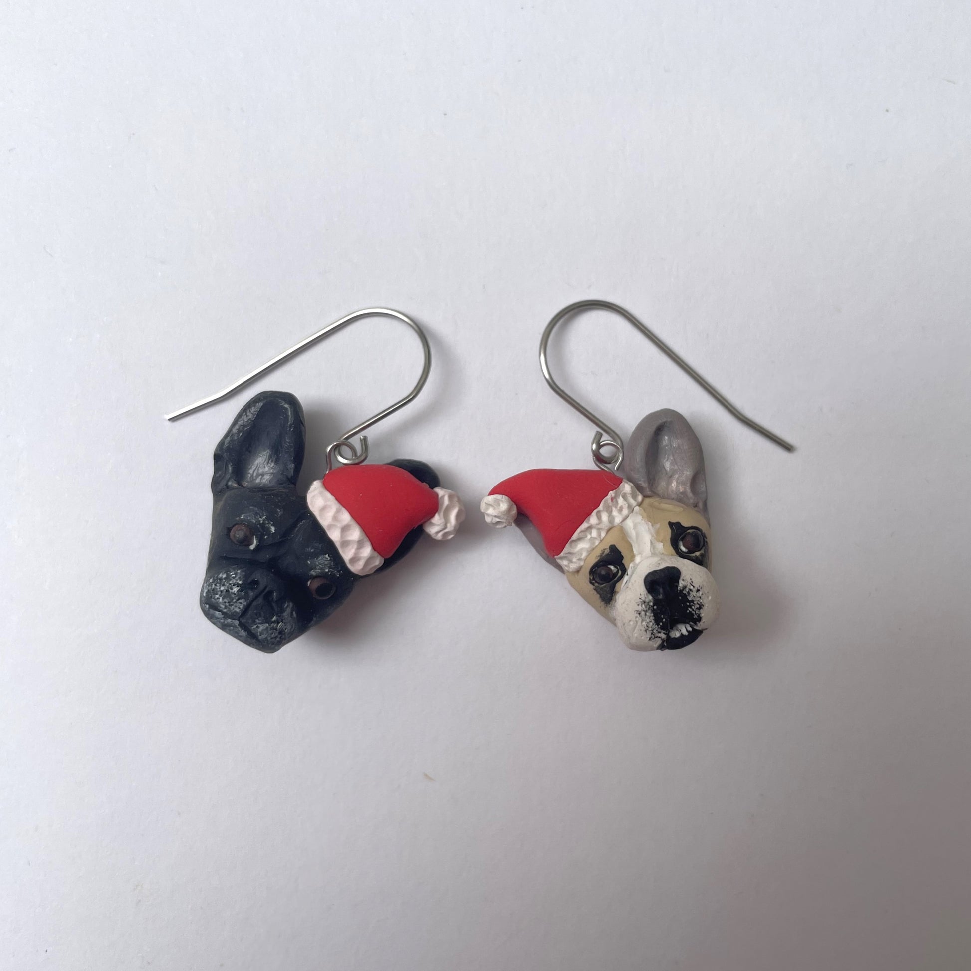 Handmade mismatched custom french bulldog hook earrings wearing santa hats.