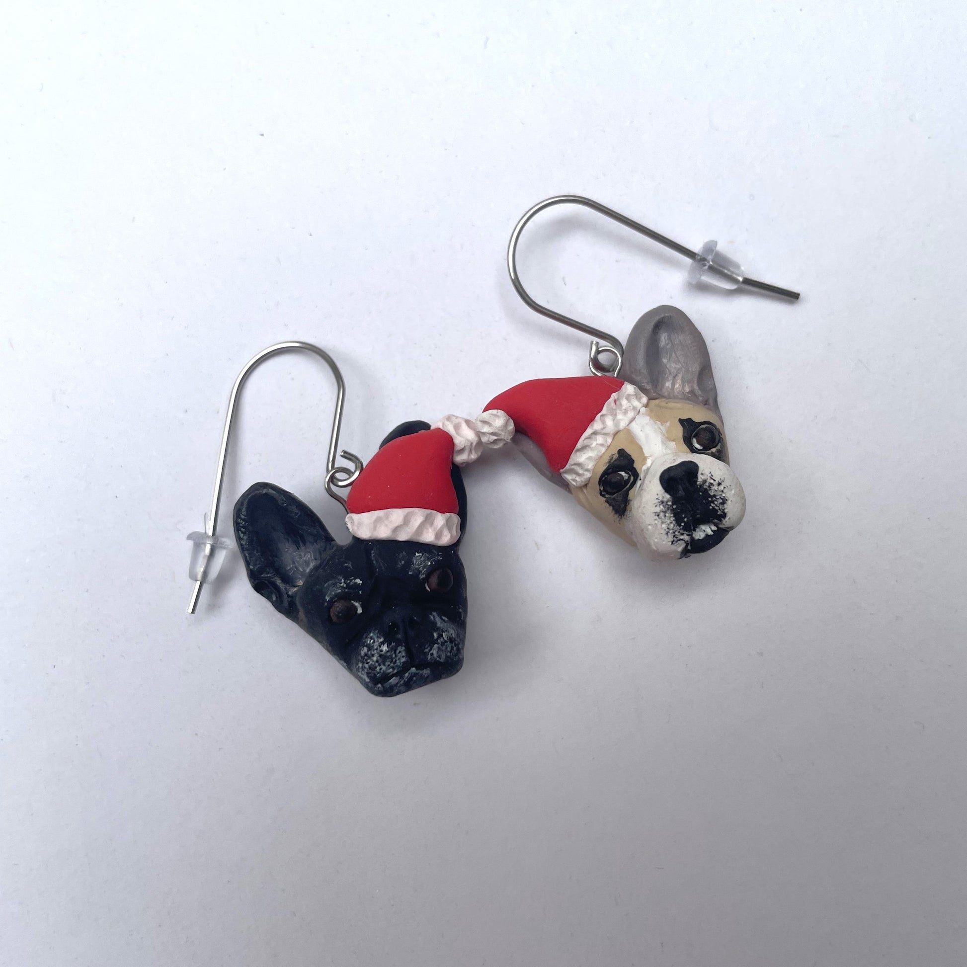 Handmade mismatched custom french bulldog hook dangle earrings wearing santa hats.