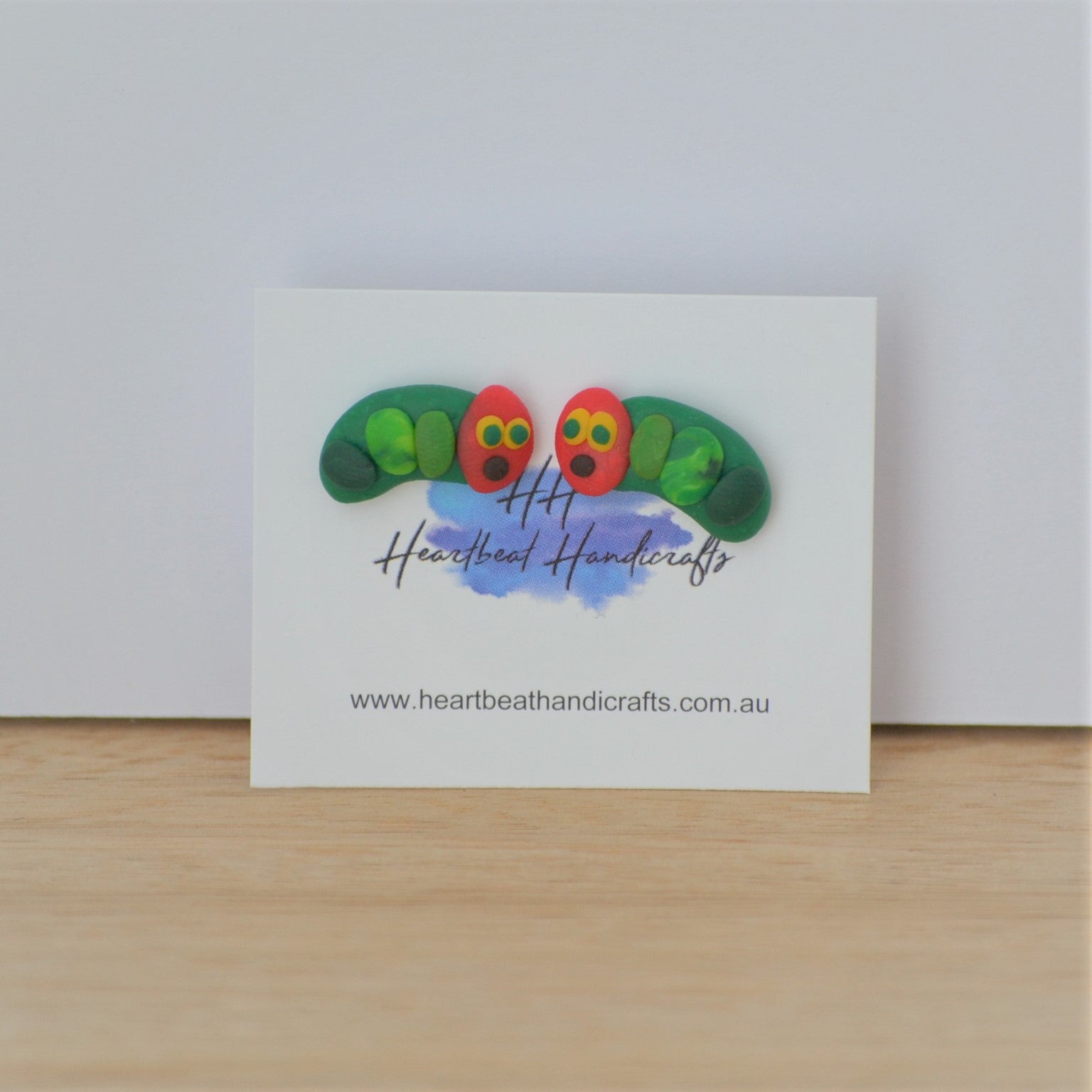 Caterpillar stud earrings shown on earrings card on timber and white background