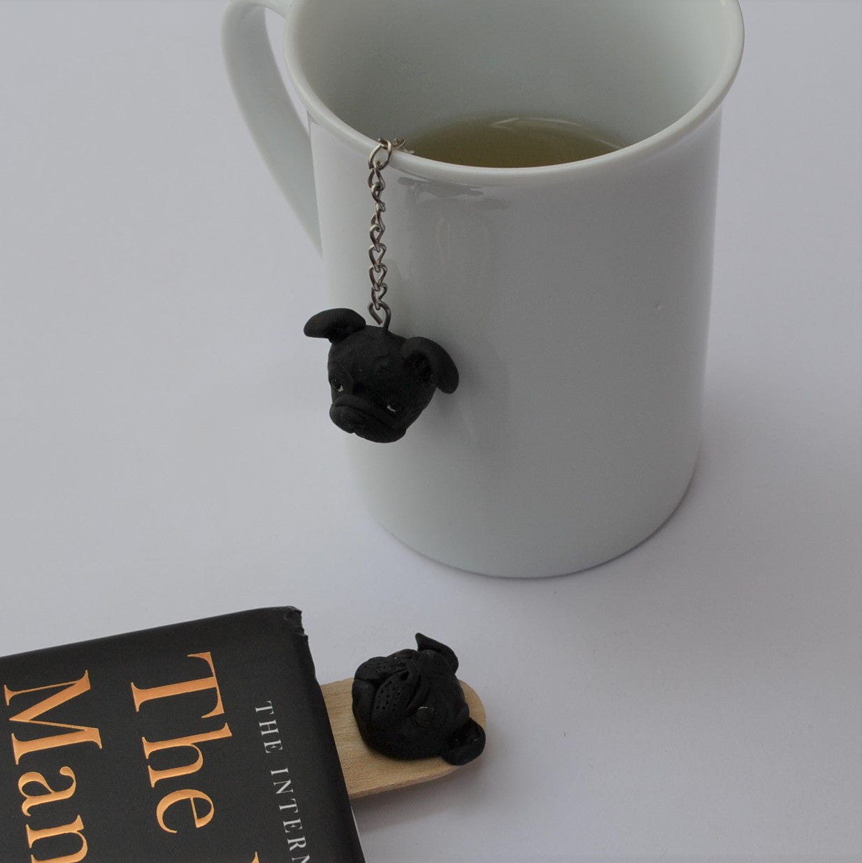 Handmade custom pet face page keeper showing a black pug's face, beside a cup of tea.