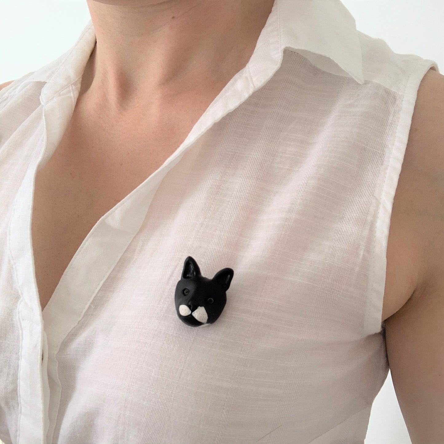 Handmade polymer clay black cat brooch, shown on white shirt.