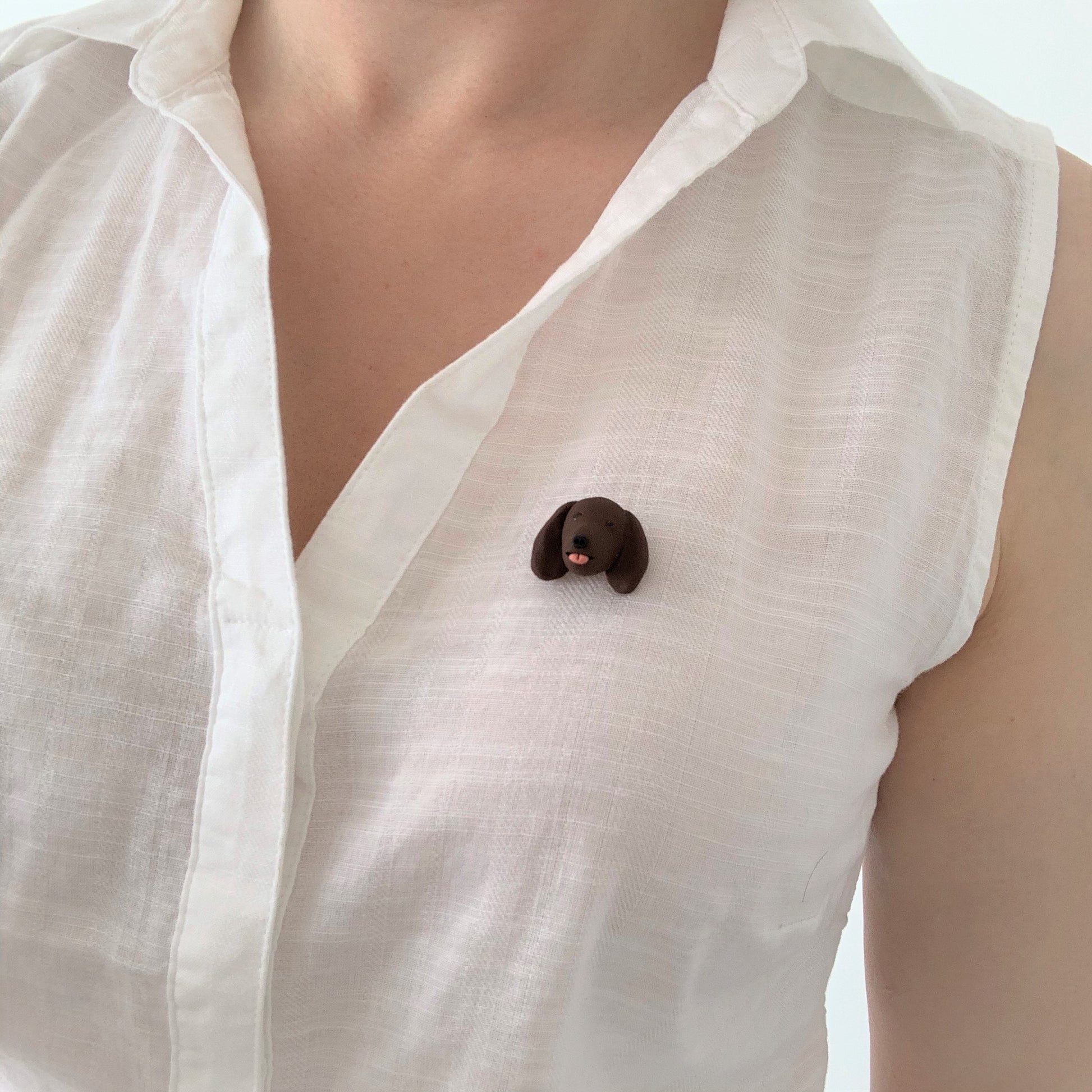 Handmade polymer clay brown dog brooch, shown on white shirt.