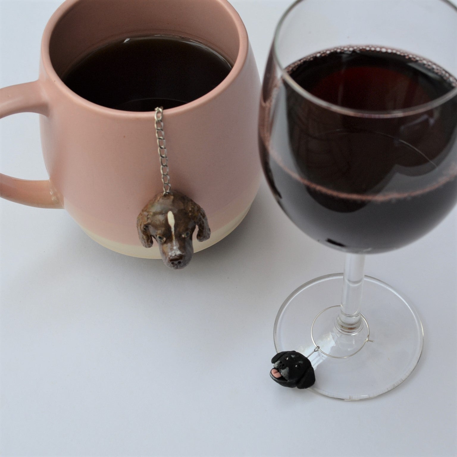 Custom dog handmade mesh ball tea strainer in use on a white mug beside dog wine charm on red wine glass