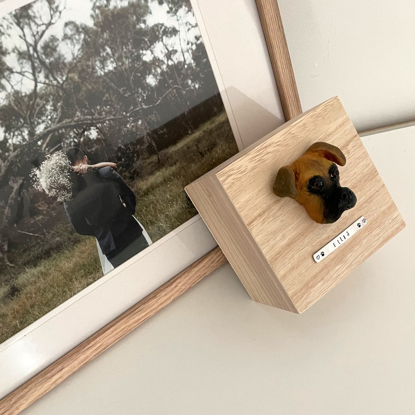 Custom timber pet memorial keepsake box with handscultped dog face on the lid, with a name plaque reading Ellis, leaning against photo frame.