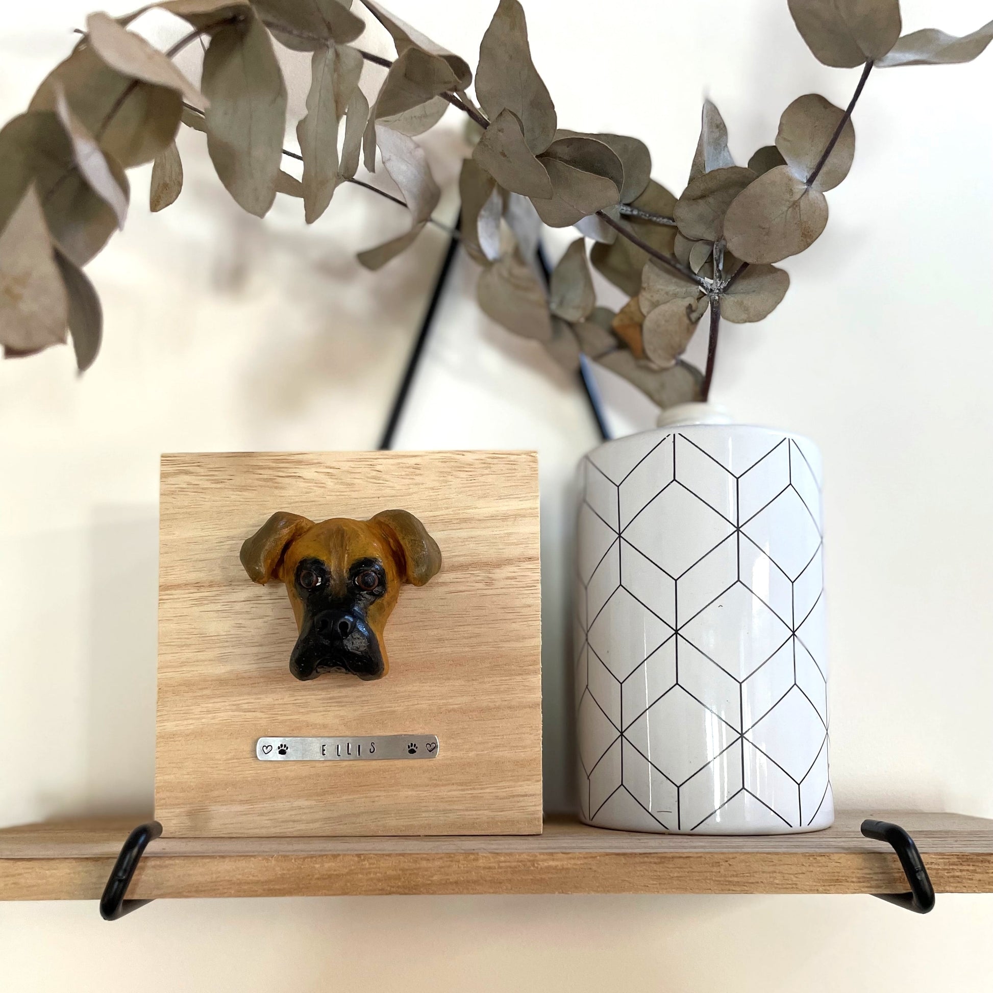 Custom timber pet memorial keepsake box with handscultped dog face on the lid, with a name plaque reading Ellis, positioned beside vase.