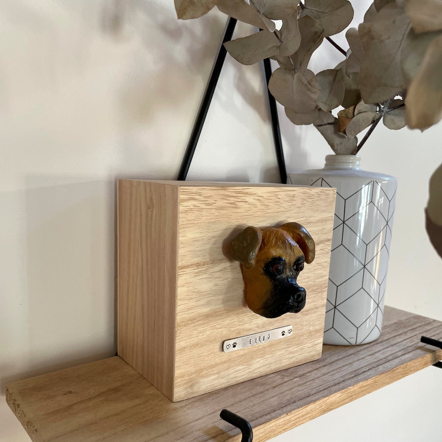 Custom timber pet memorial keepsake box with handscultped dog face on the lid, with a name plaque reading Ellis, sitting on a shelf.
