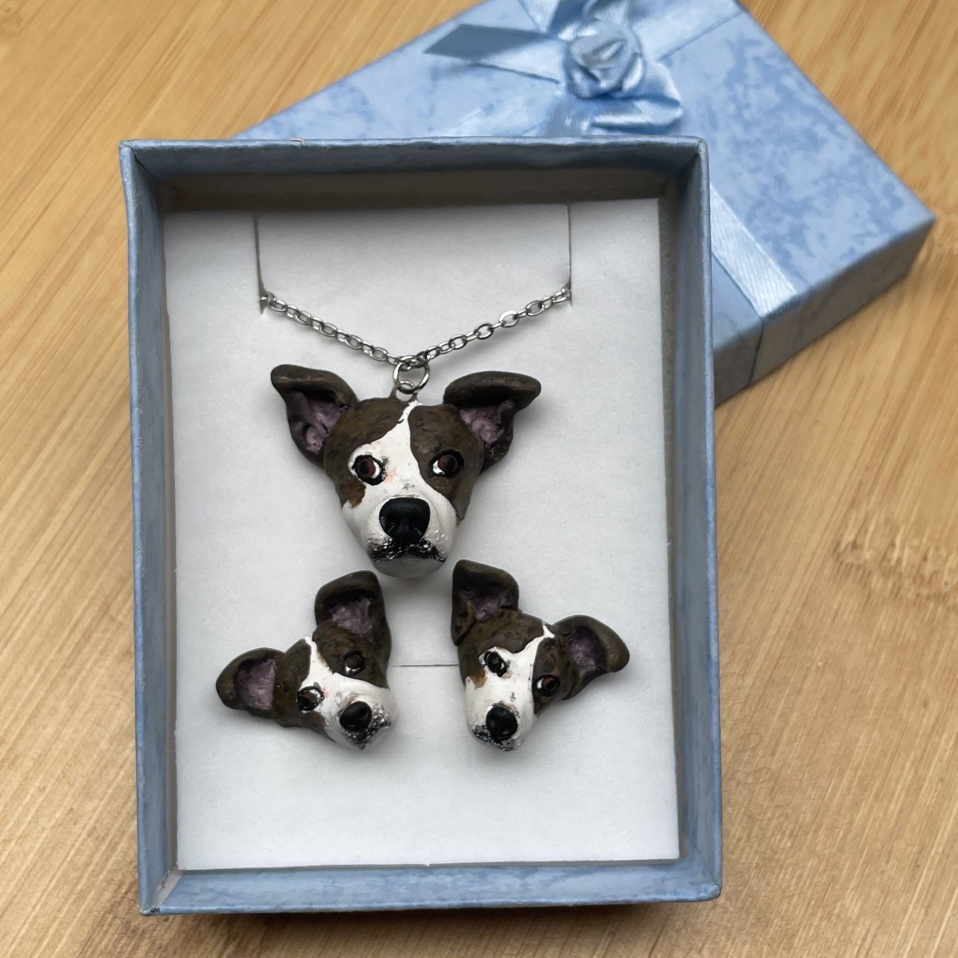 Handmade custom dog necklace pendant on chain and matching stud earrings, in blue display box on timber background.