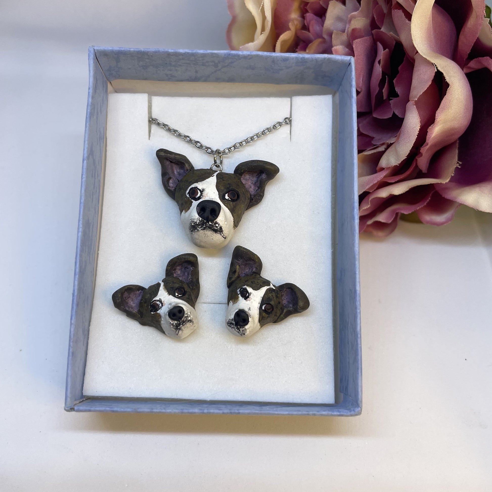 Handmade custom dog necklace pendant on chain plus matching stud earrings, in blue display box in front of faux pink flower.