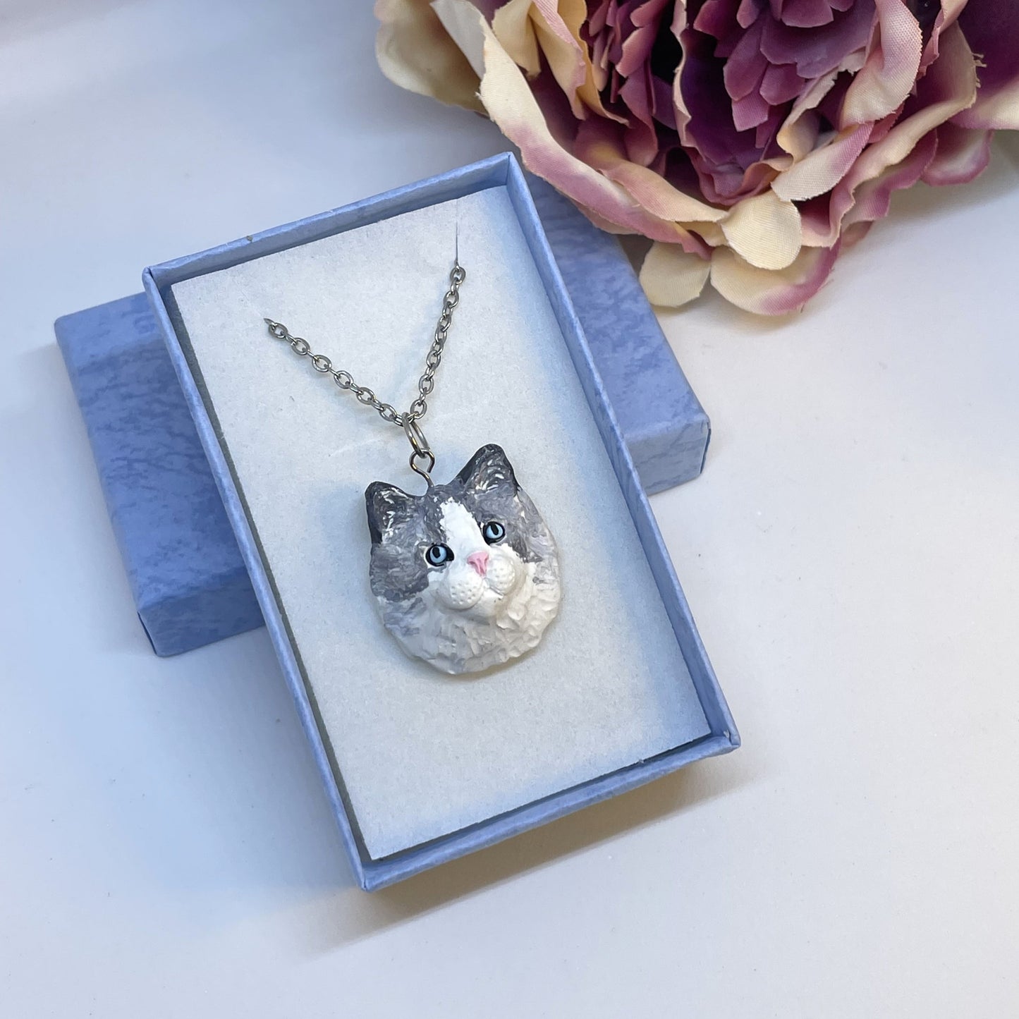 Handmade custom cat necklace pendant on chain, in blue display box in front of faux pink flower.