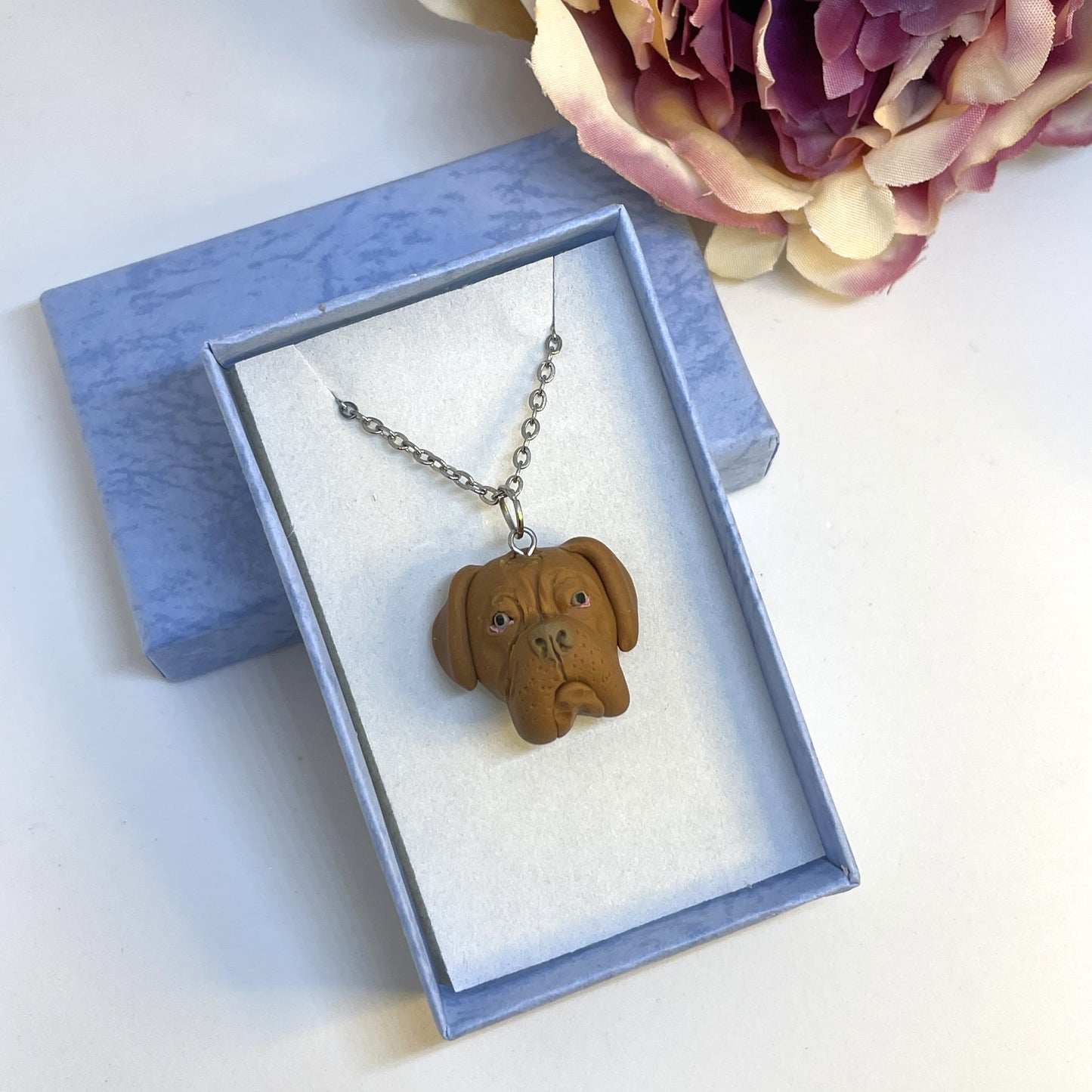 Handmade custom Dogue De Bordeaux necklace pendant on chain, in blue display box in front of faux pink flower.