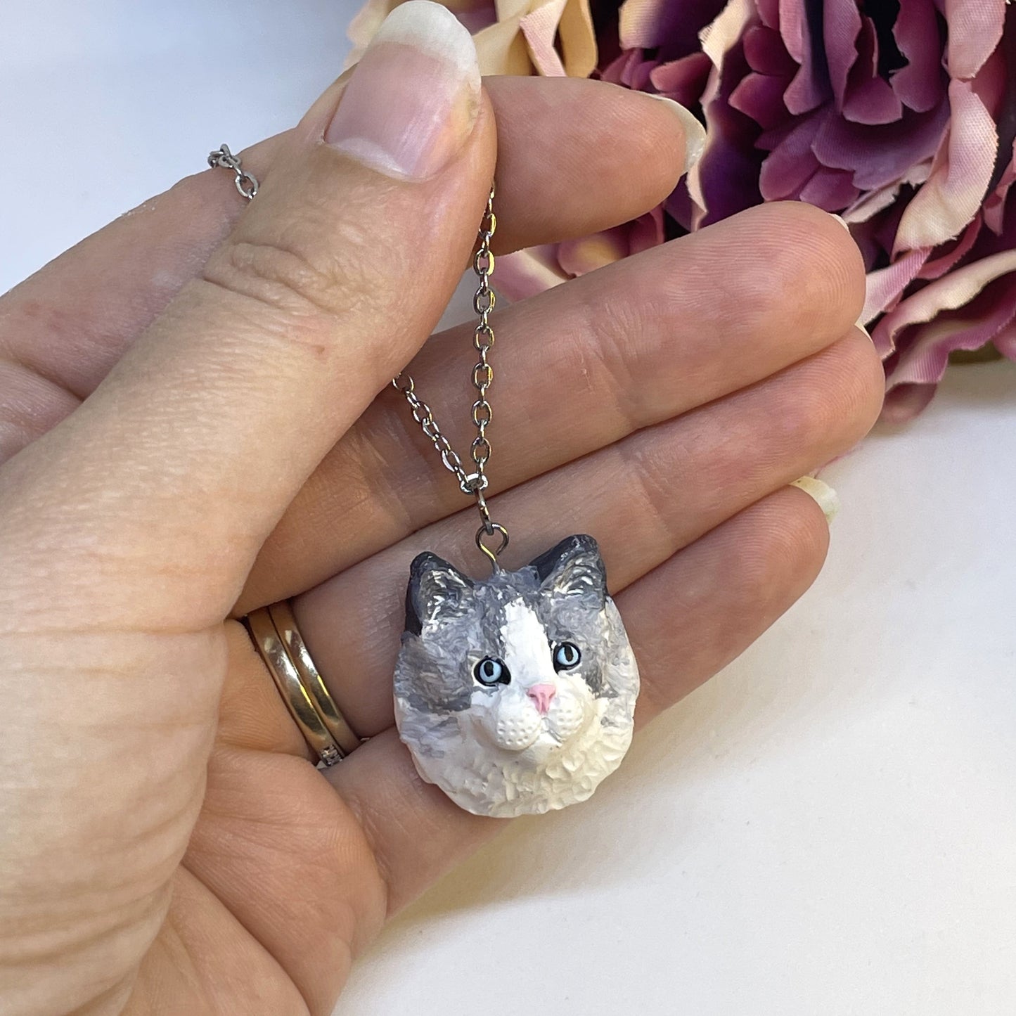 Handmade custom cat necklace pendant on chain, held in front of faux pink flower.