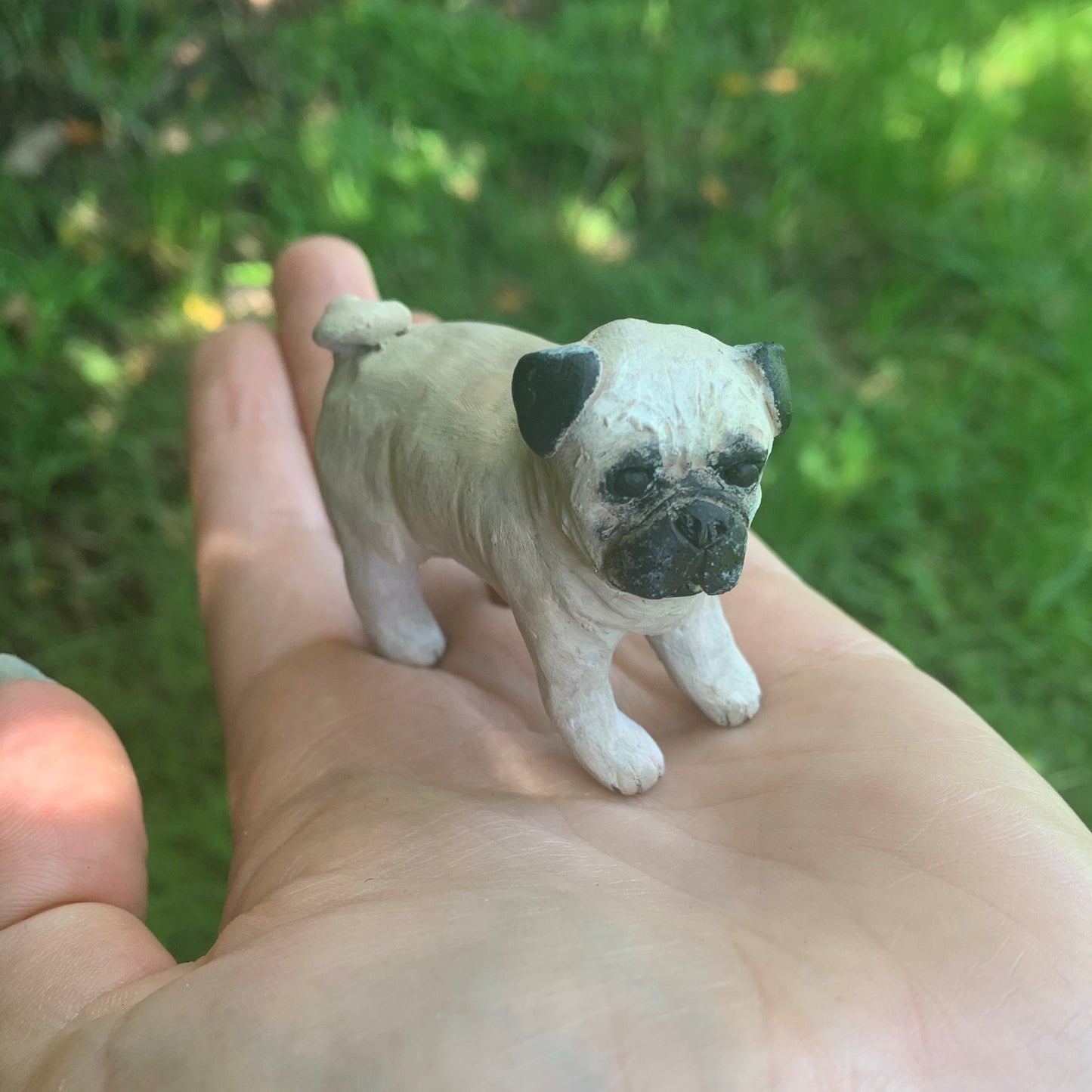 Handmade polymer clay mini pug dog figurine standing on a hand.