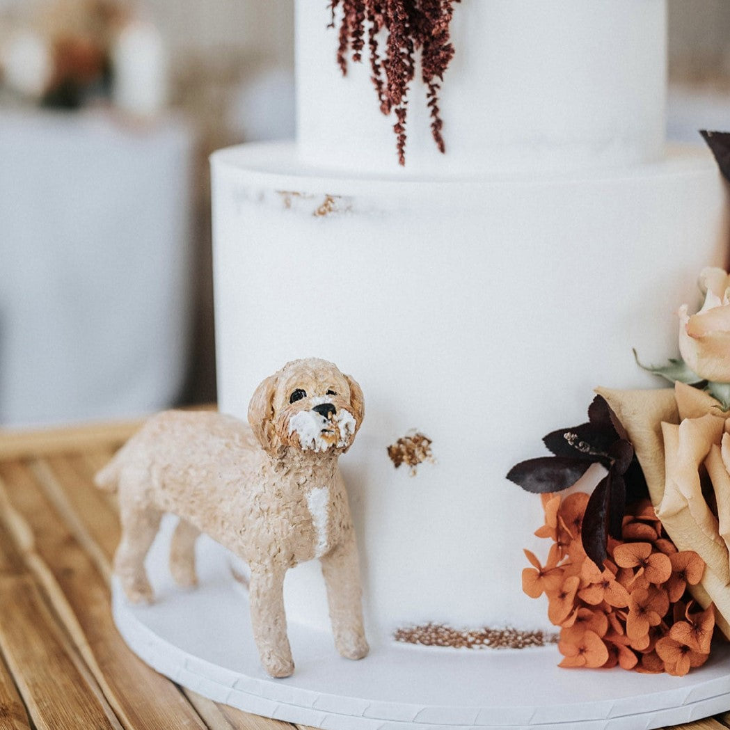 Handmade dog figuring standing beside wedding cake, staged to look like it has taken a bite of the cake.