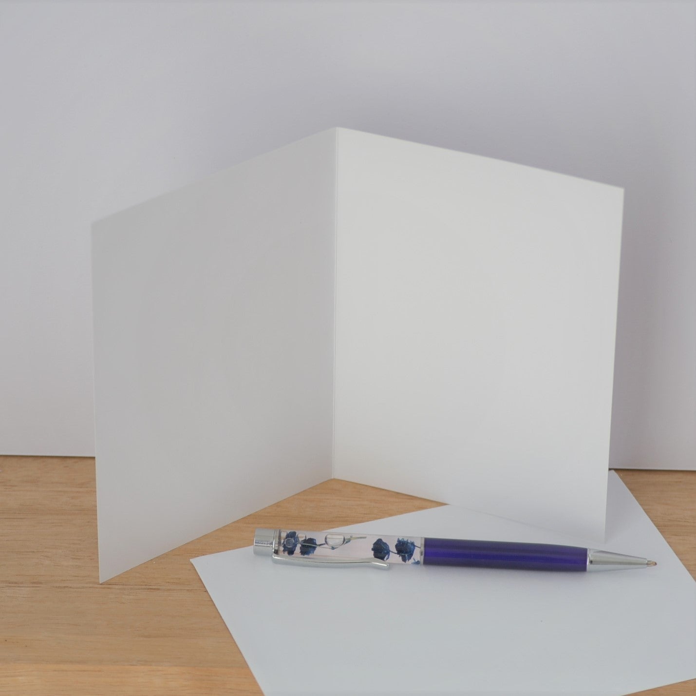 Open blank greeting card standing on timber, with blue pen at base