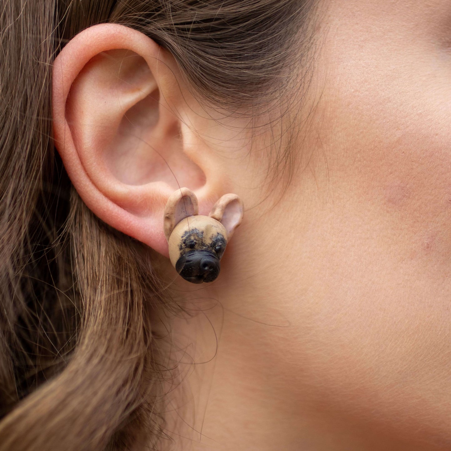 Handmade polymer clay french bulldog stud earrings shown on model's ear