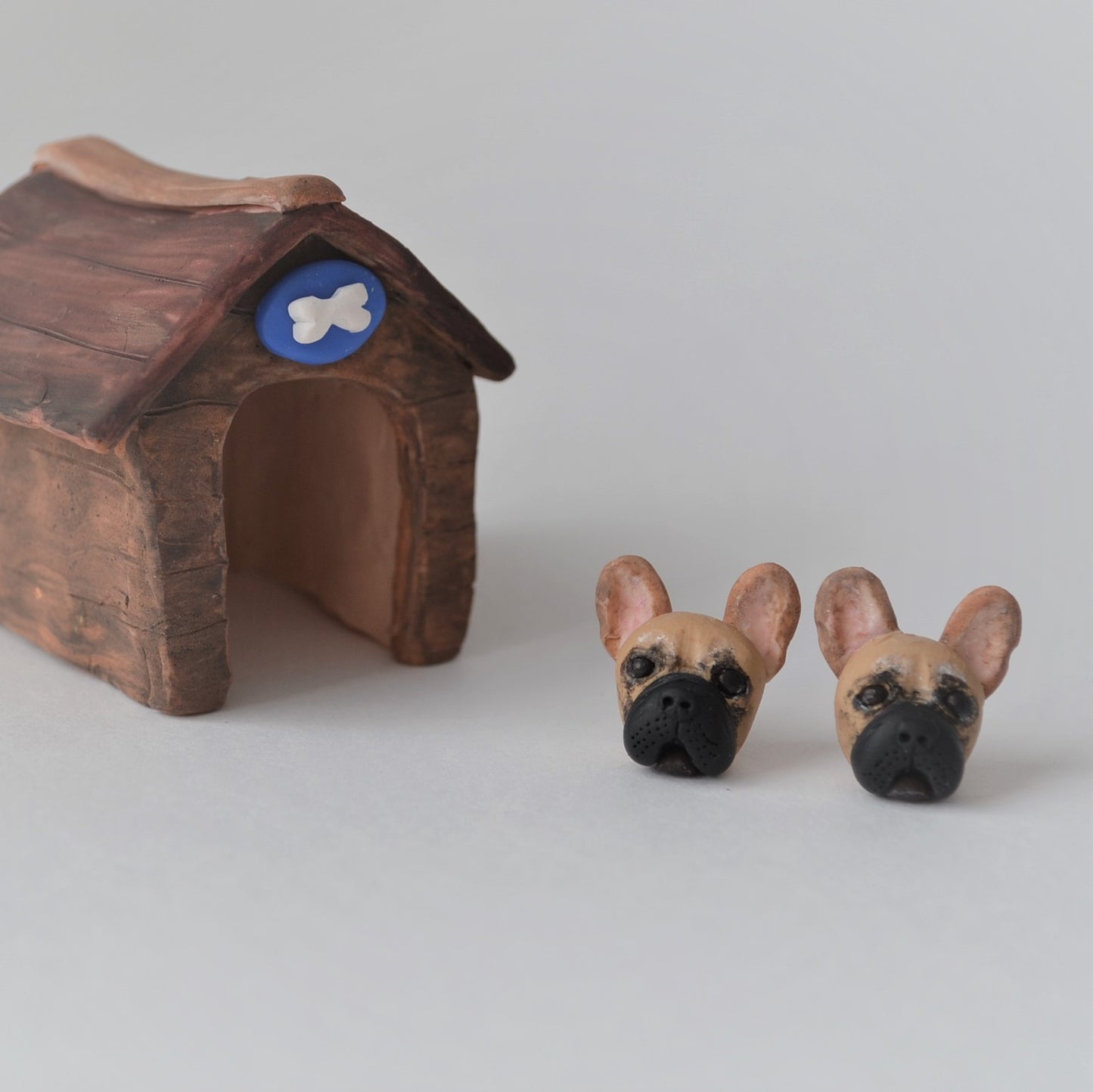 Handmade polymer clay french bulldog stud earrings shown beside mini kennel