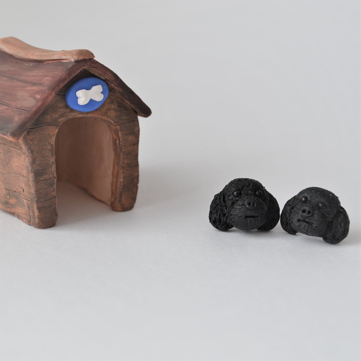 Handmade polymer clay black poodle stud earrings shown beside mini kennel