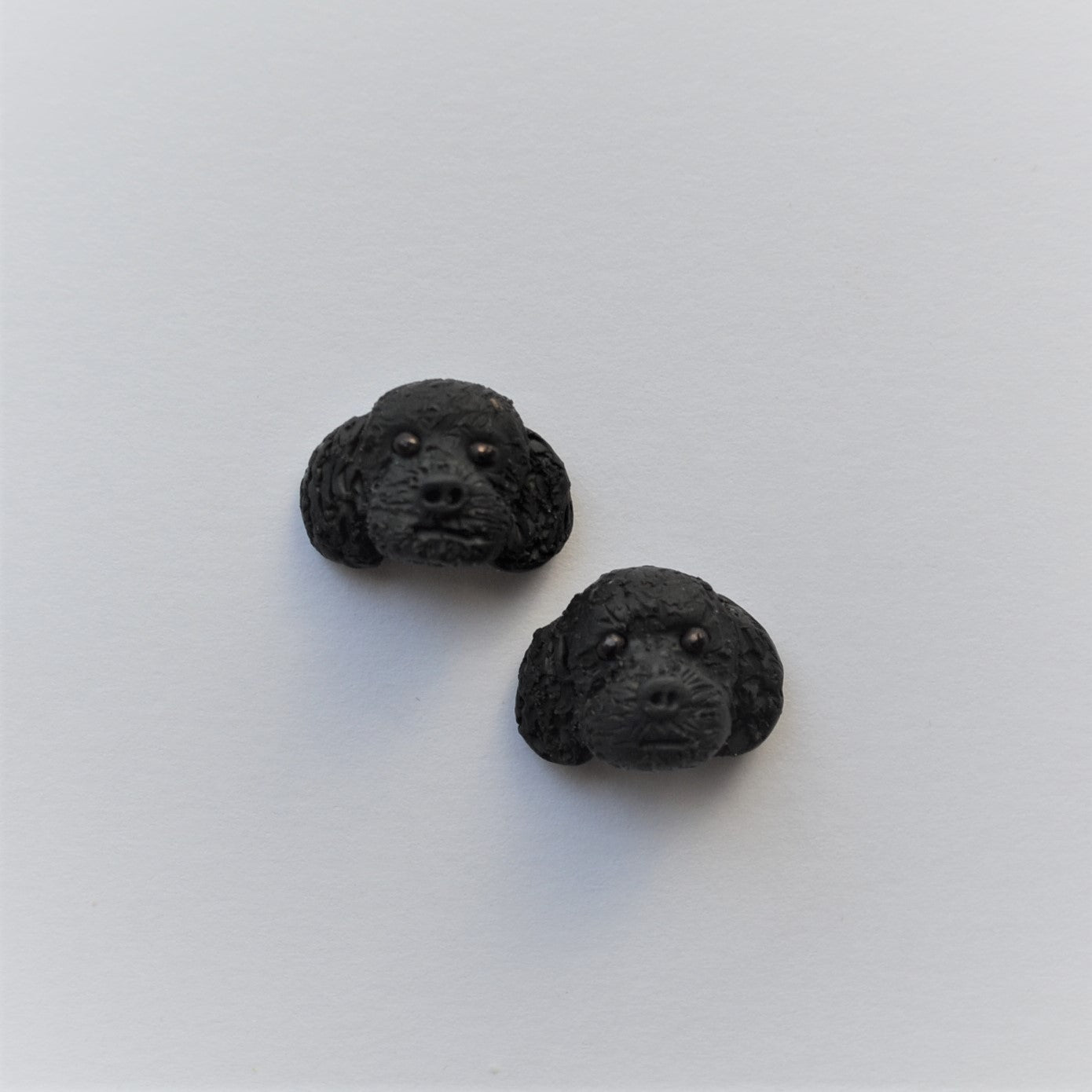 Handmade polymer clay black poodle stud earrings shown offset on white background