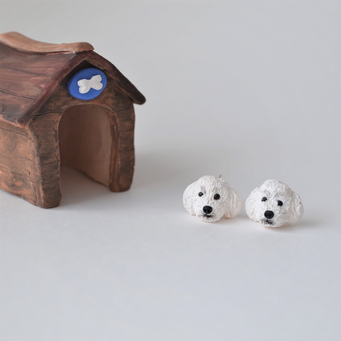 Handmade polymer clay white poodle stud earrings shown beside kennel