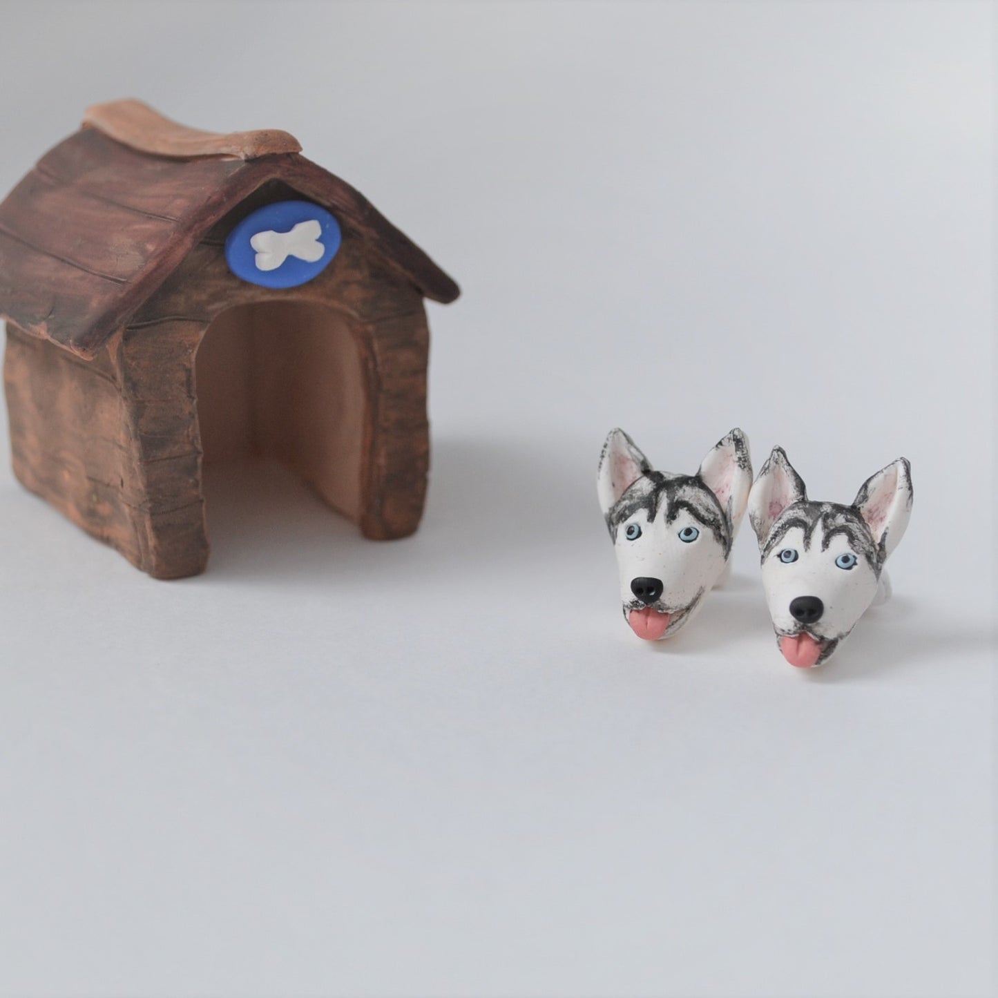 Handmade polymer clay husky stud earrings shown styled beside mini kennel
