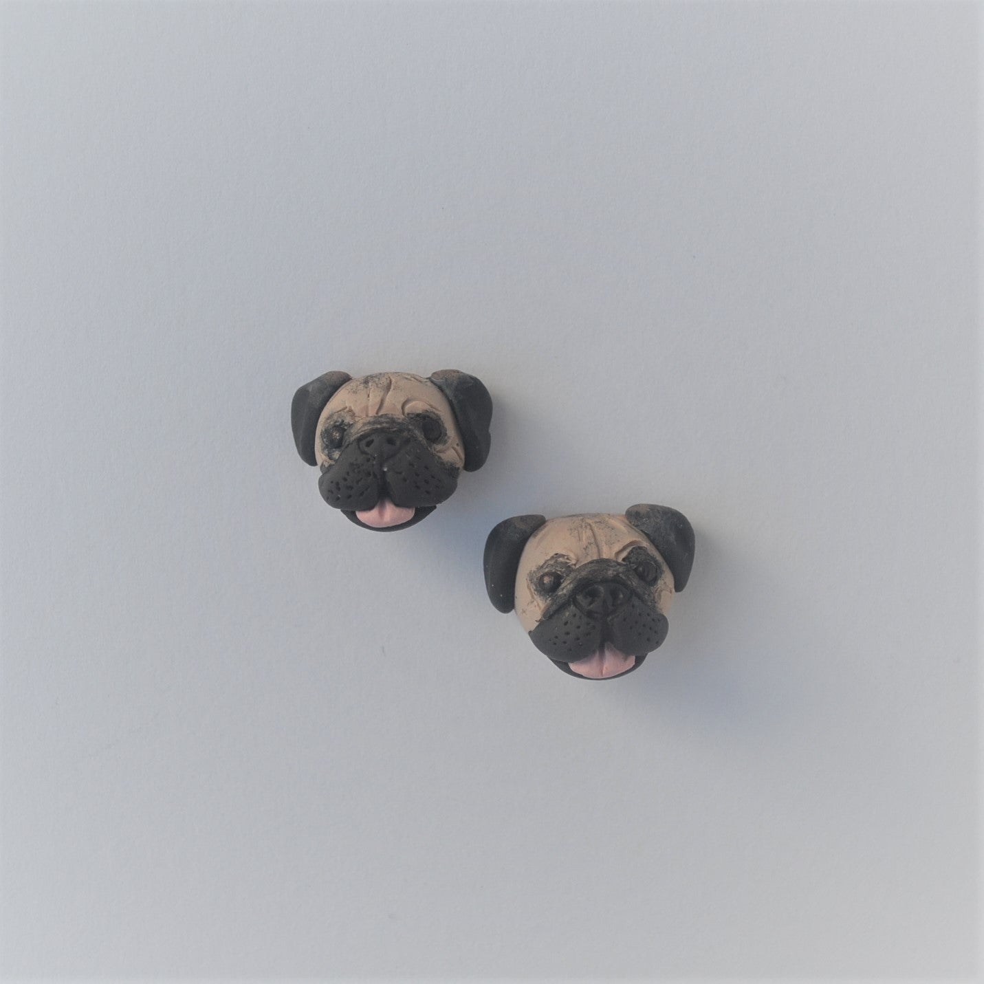 Handmade polymer clay pug stud earrings shown offset on white background