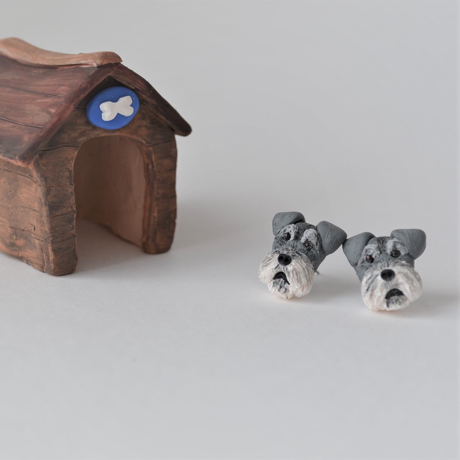 Handmade polymer clay schnauzer stud earrings shown beside mini kennel