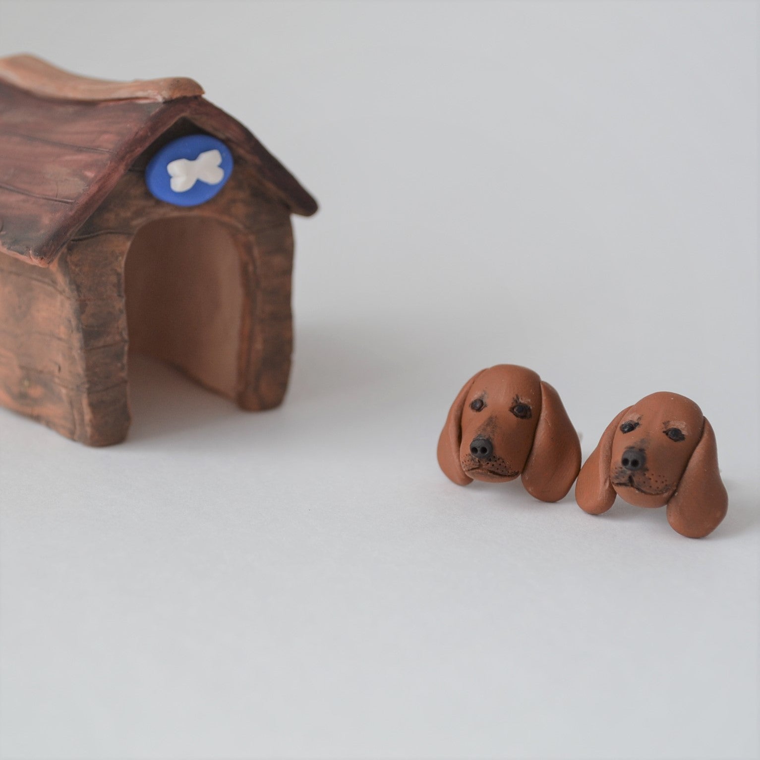 Handmade polymer clay Dachshund stud earrings shown beside mini kennel