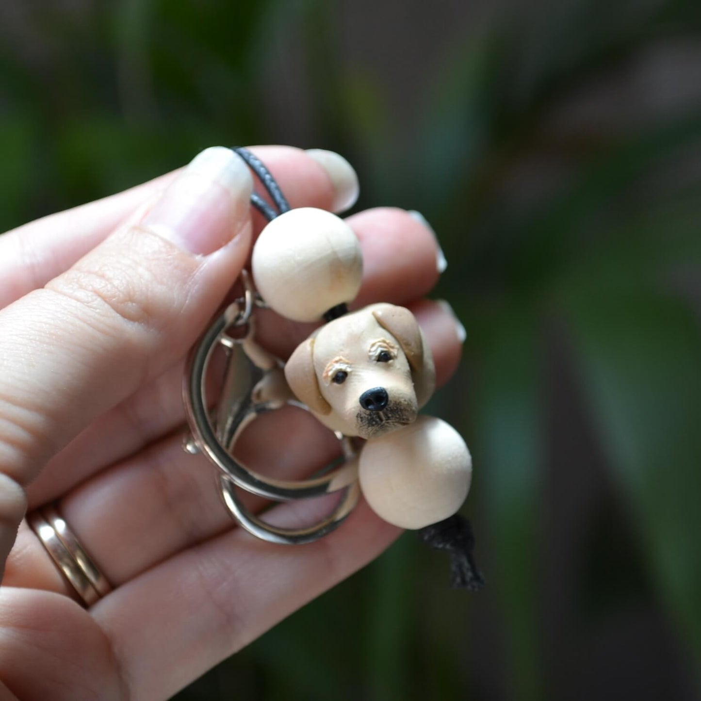 Handmade timber and polymer clay golden retriever dog keychain being held in front of green palm plant background