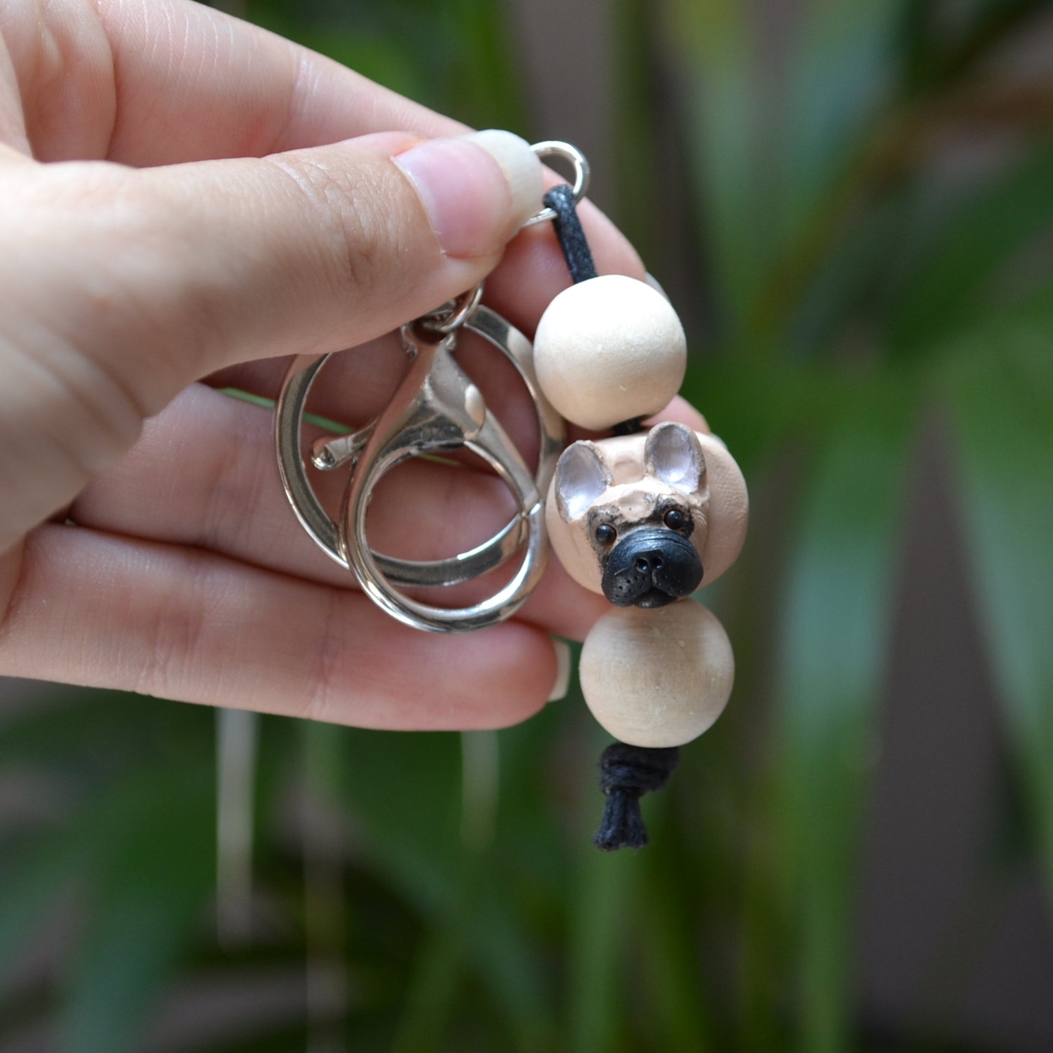Handmade timber and polymer clay french bulldog keychain being held in front of green palm plant background