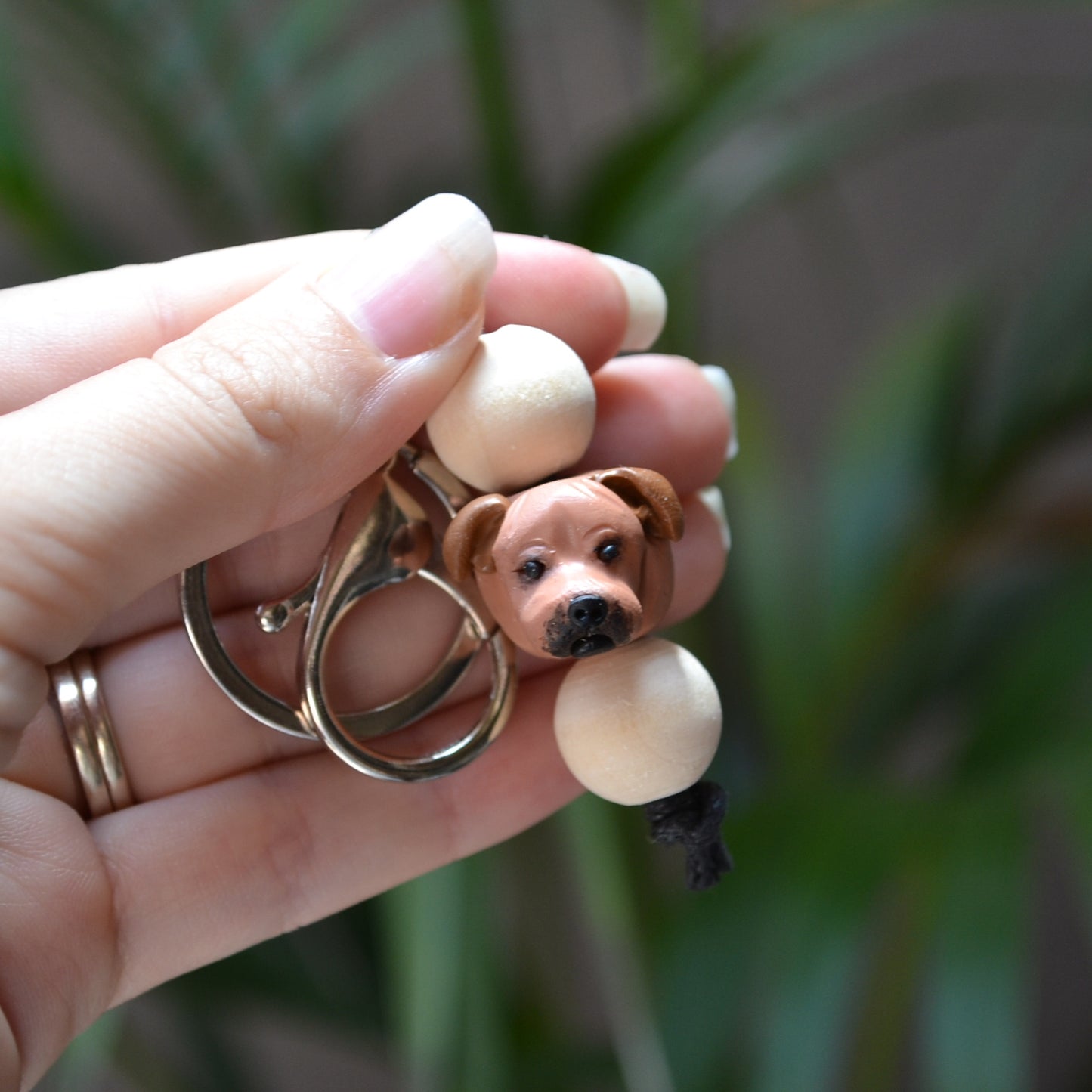 Handmade timber and polymer clay staffy dog keychain being held in front of green palm plant background