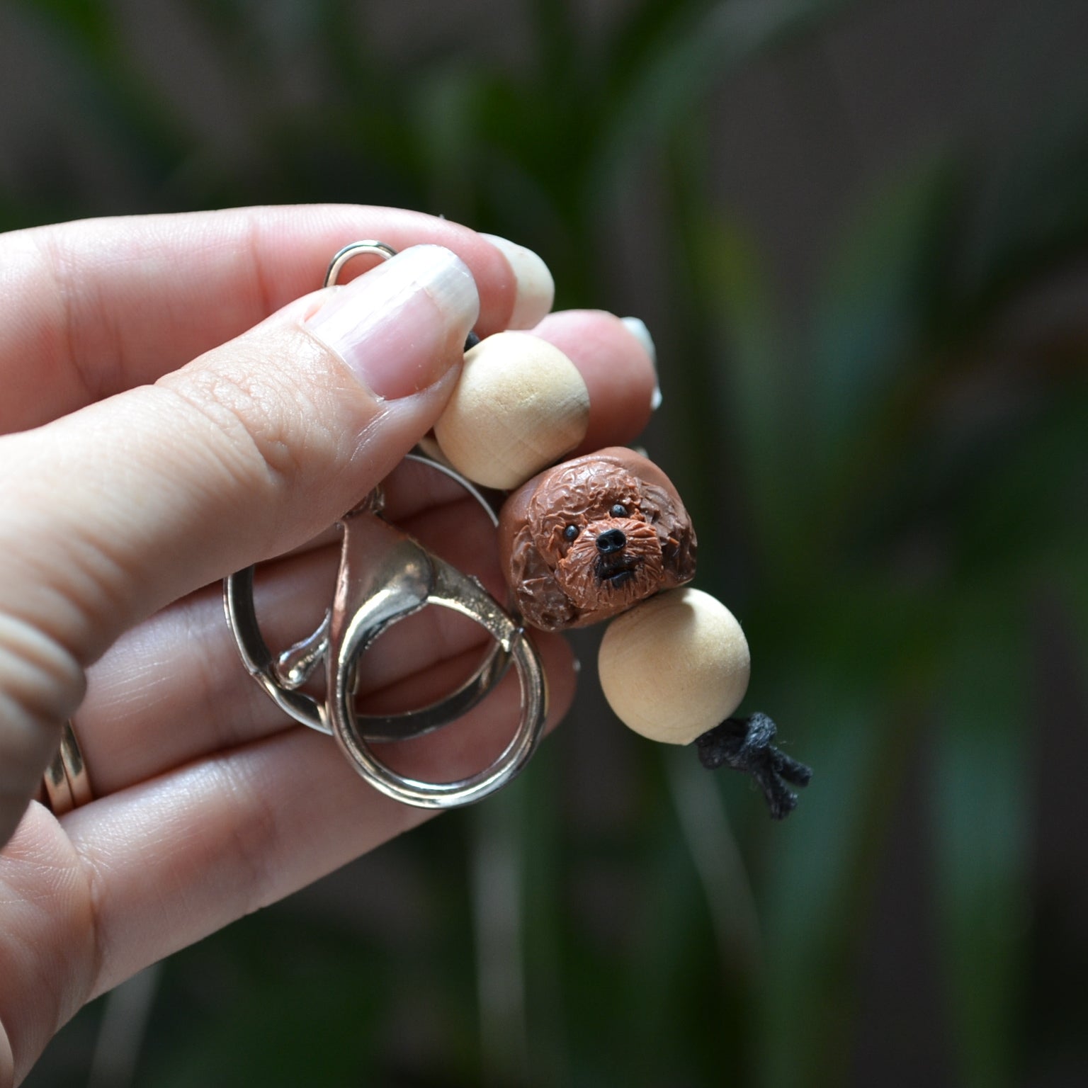 Handmade timber and polymer clay cavoodle dog keychain being held in front of green palm plant background