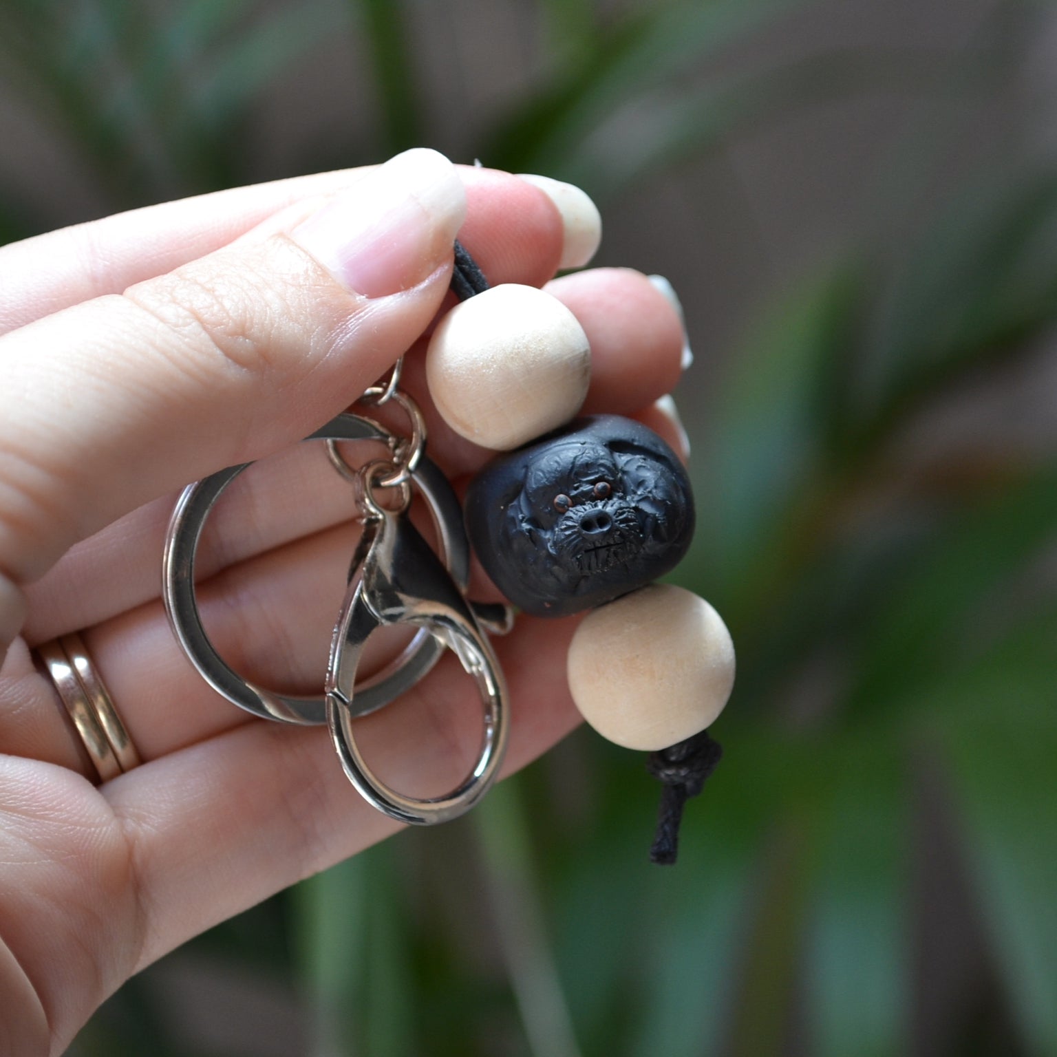 Handmade timber and polymer clay black poodle keychain being held in front of a green palm plant background.