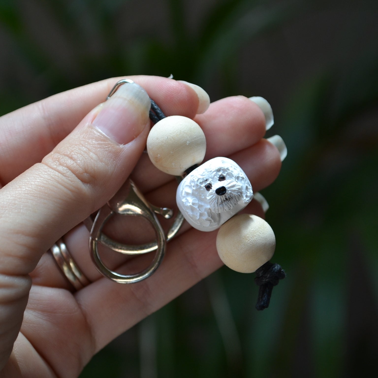 Handmade timber and polymer clay white poodle dog keychain being held in front of green palm plant background