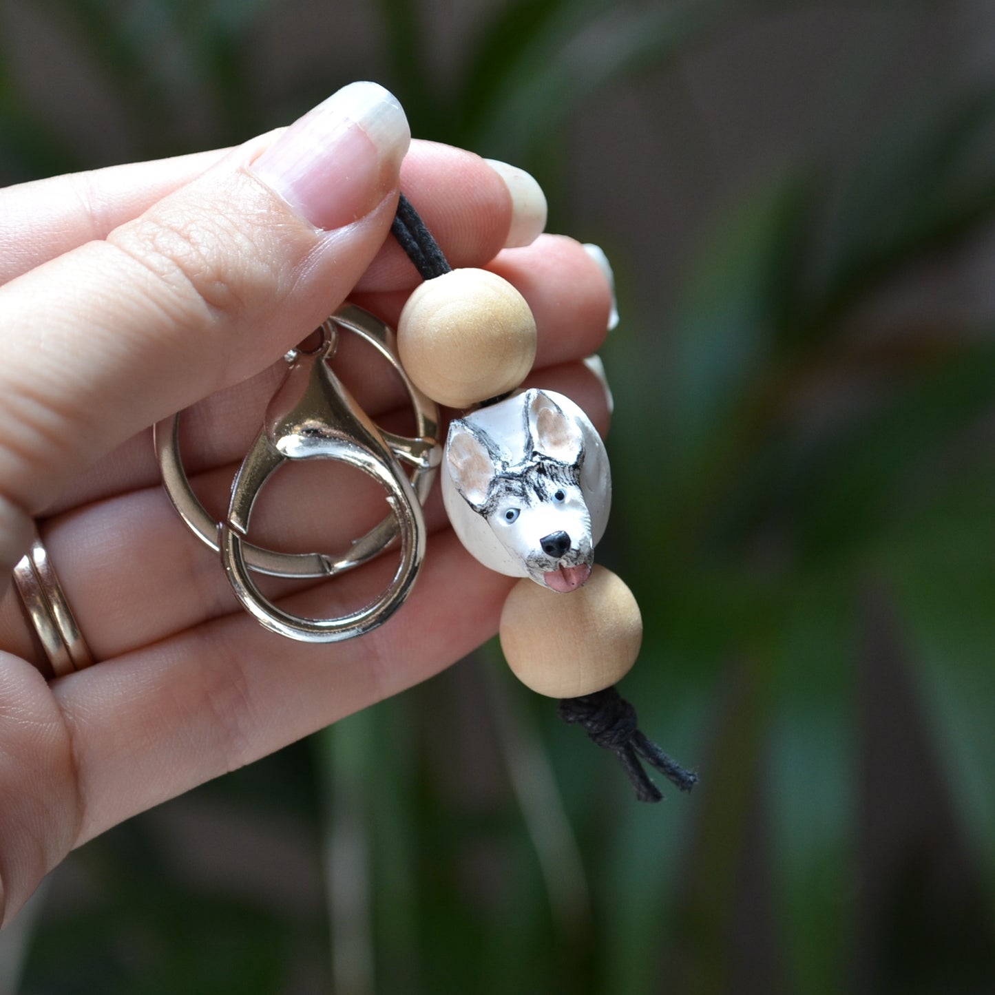 Handmade timber and polymer clay husky dog keychain being held in front of green palm plant background