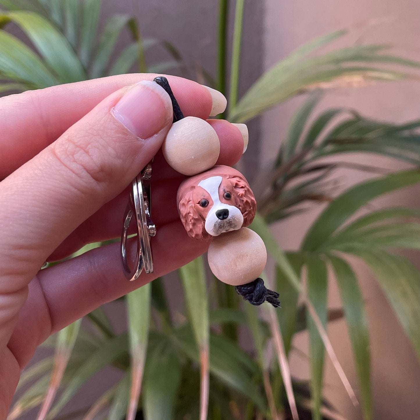 Polymer clay and timber handmade dog keyrings held in front of green palm plant background