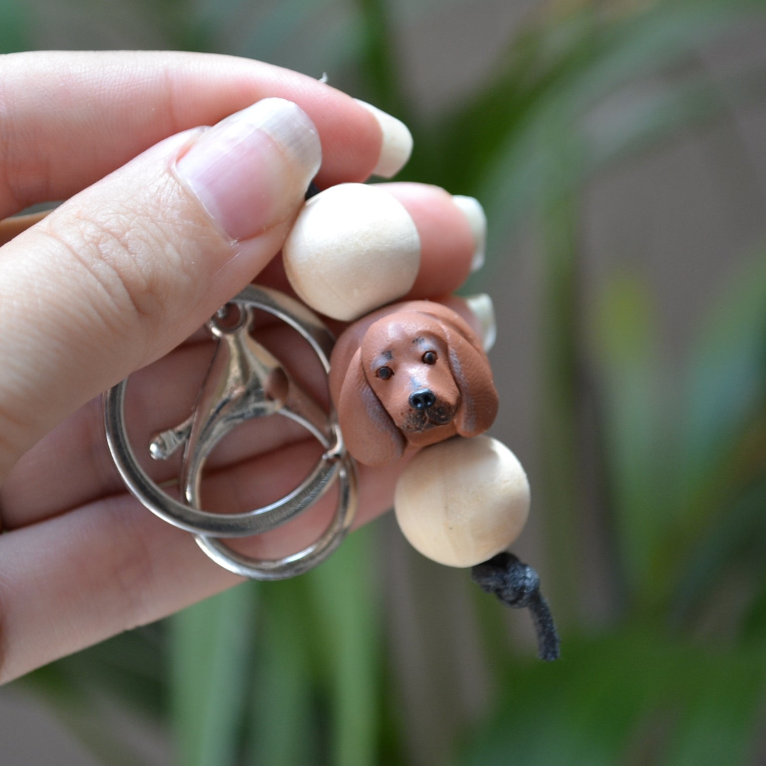 Handmade timber and polymer clay dachshund dog keychain being held in front of green palm plant background