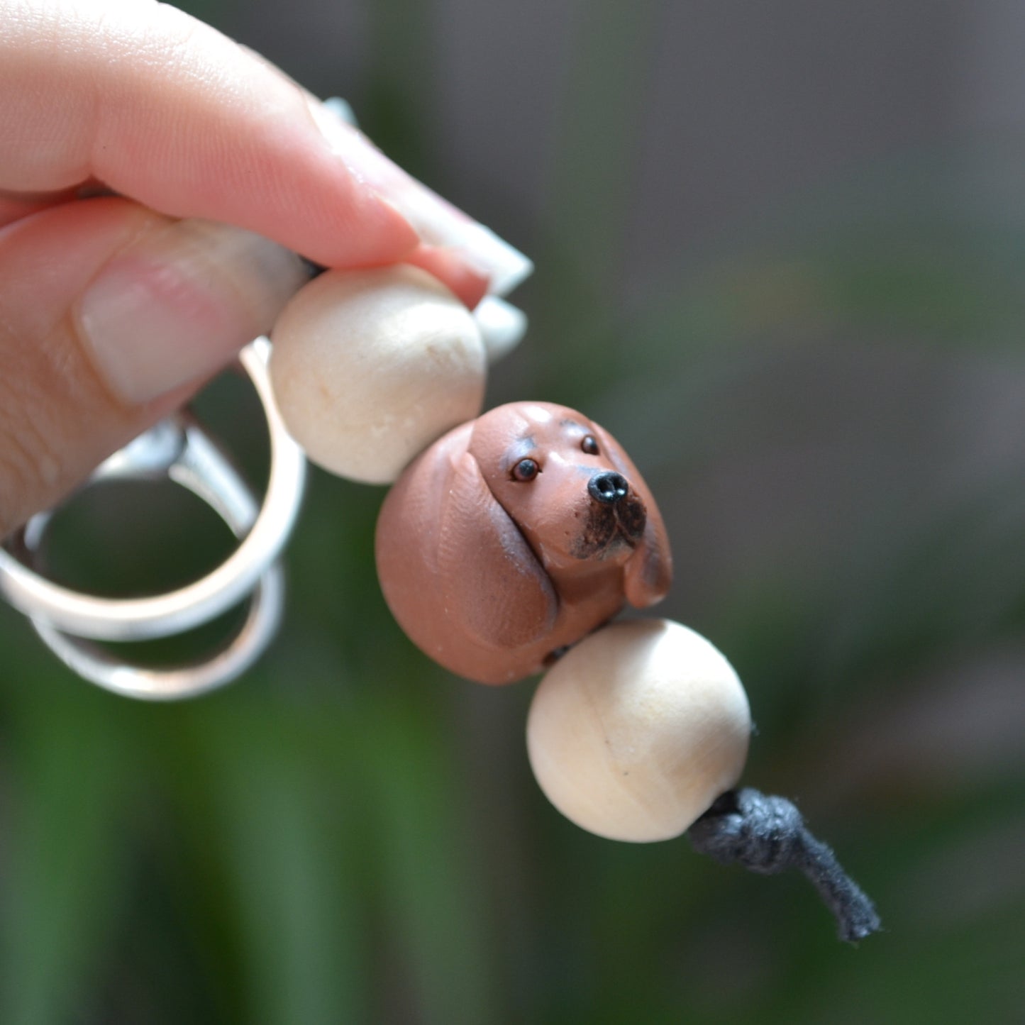 Handmade timber and polymer clay dachshund dog keychain being held in front of green palm plant background