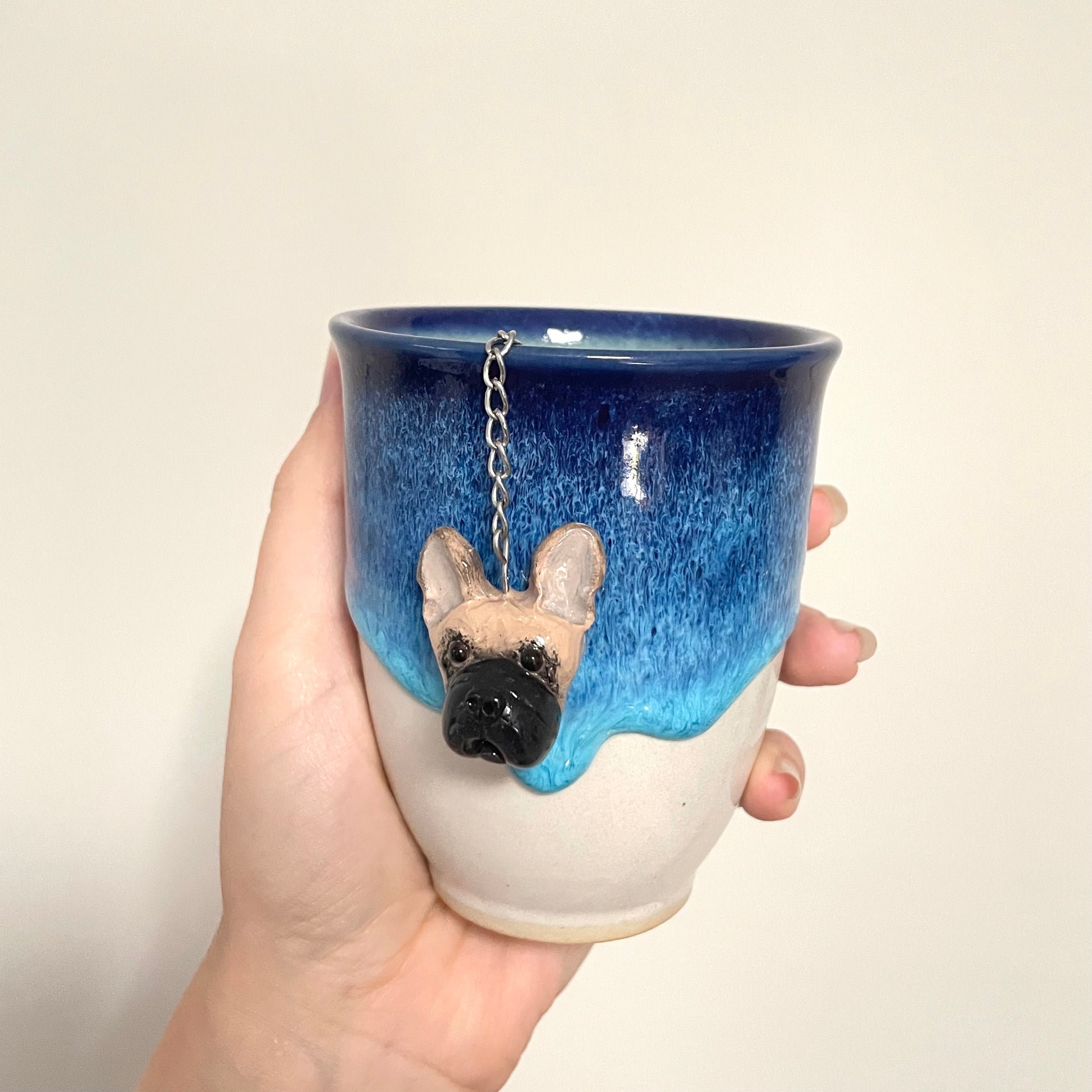 Handmade custom pet face mesh ball tea strainer being used in a blue ceramic cup.