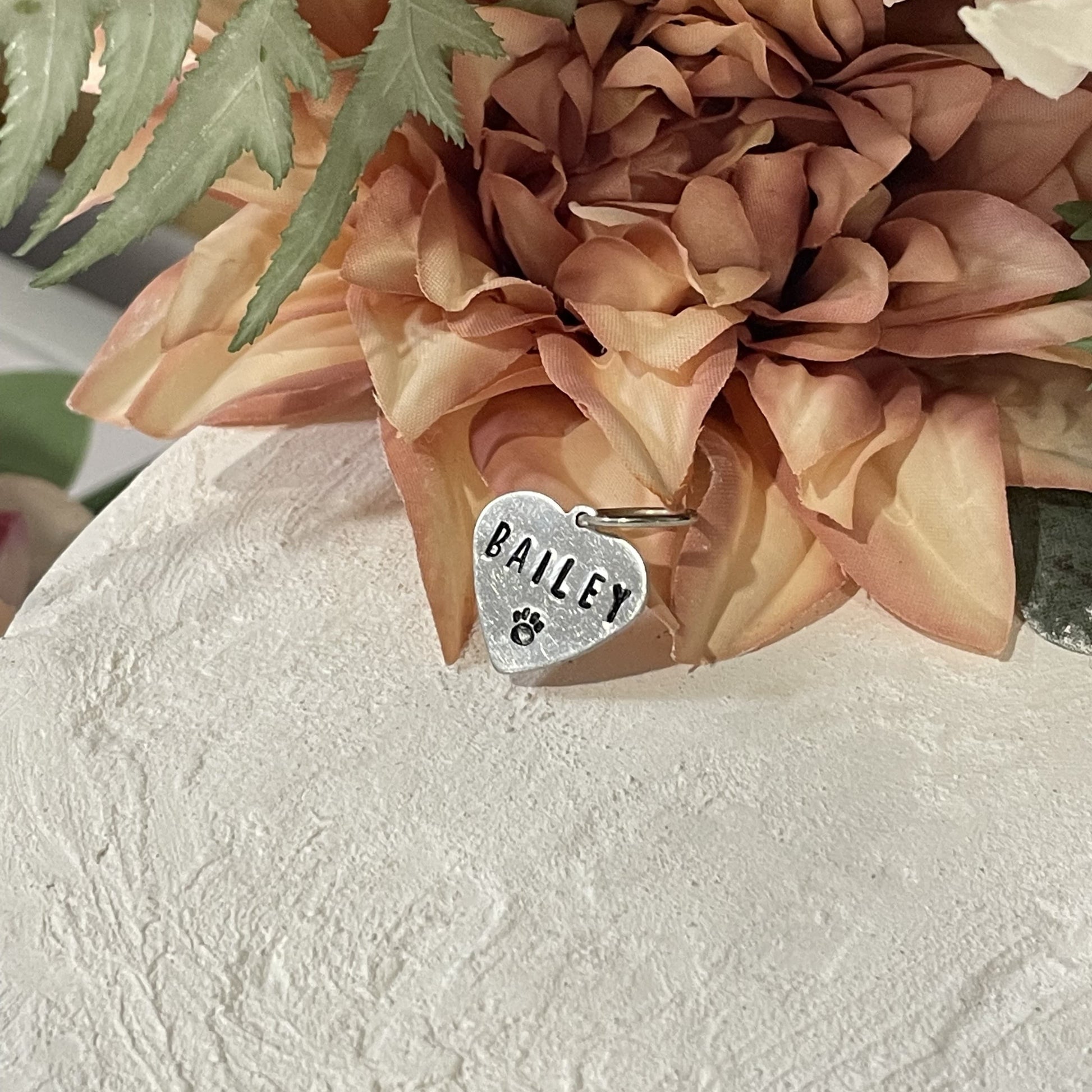 Metal hand-stamped bouquet pendant charm leaning on artificial flower, displaying the name Bailey.