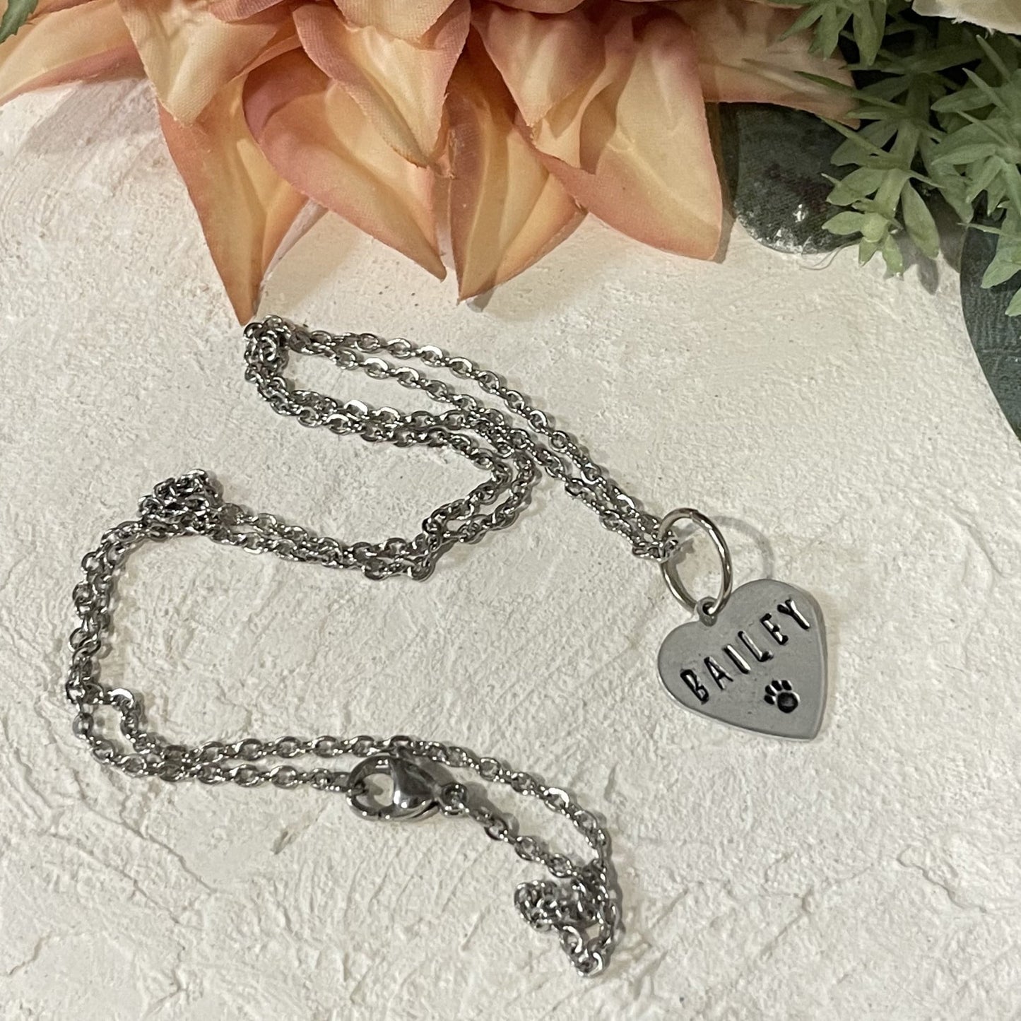 Metal hand-stamped bouquet pendant charm hanging on silver necklace chain, displaying the name Bailey.