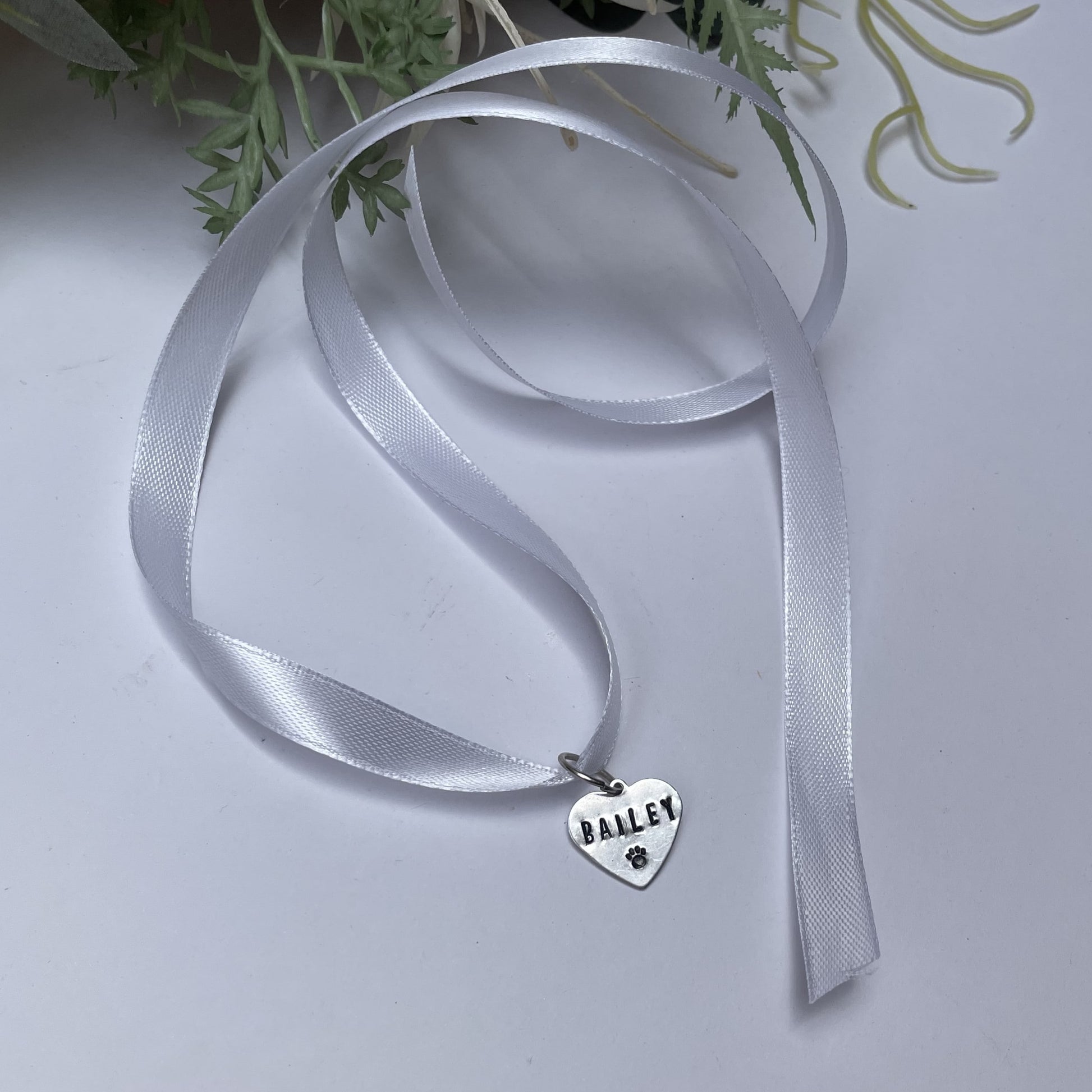 Metal hand-stamped bouquet pendant charm hanging on white ribbon, displaying the name Bailey.