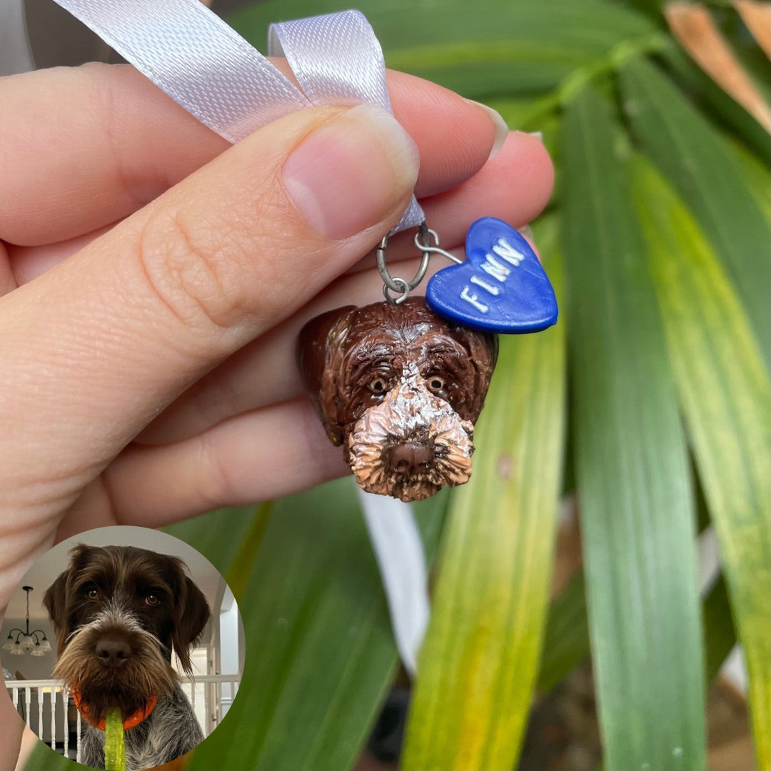 Handmade dog face pendant and blue heart charm, resembling a secondary photo of the dog. Pendants are hung on a ribbon intended to be placed on a wedding bouquet.